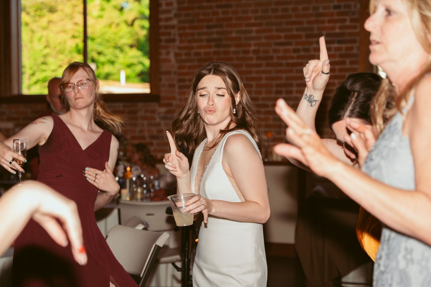 Party guests dance enthusiastically at a wedding reception in an industrial brick venue.