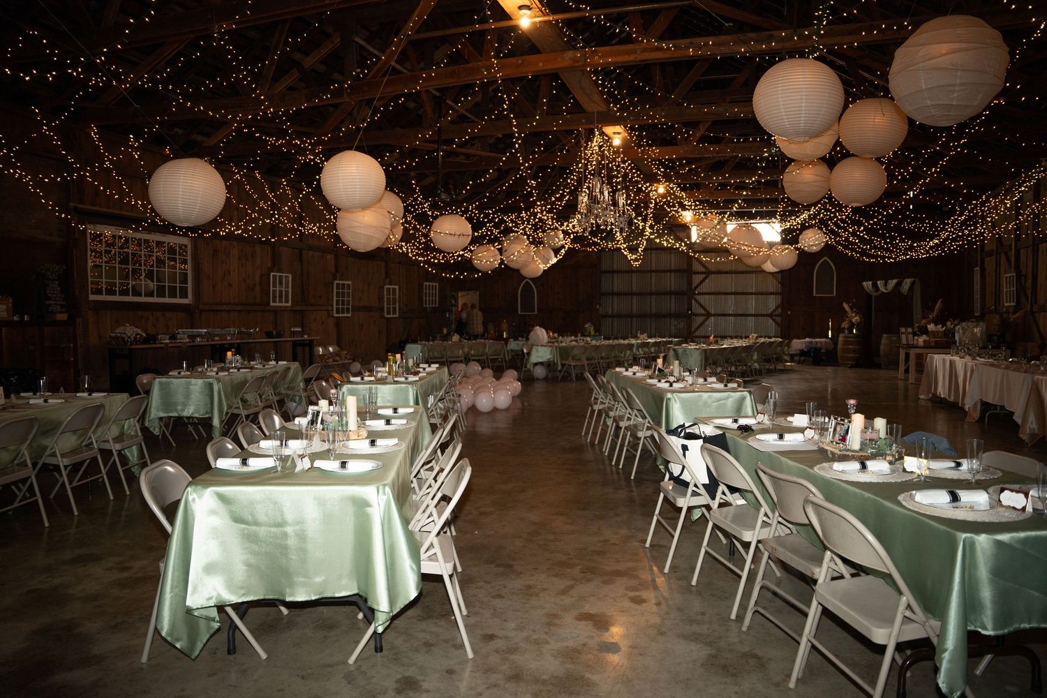 Rustic barn reception venue decorated with string lights and white paper lanterns.
