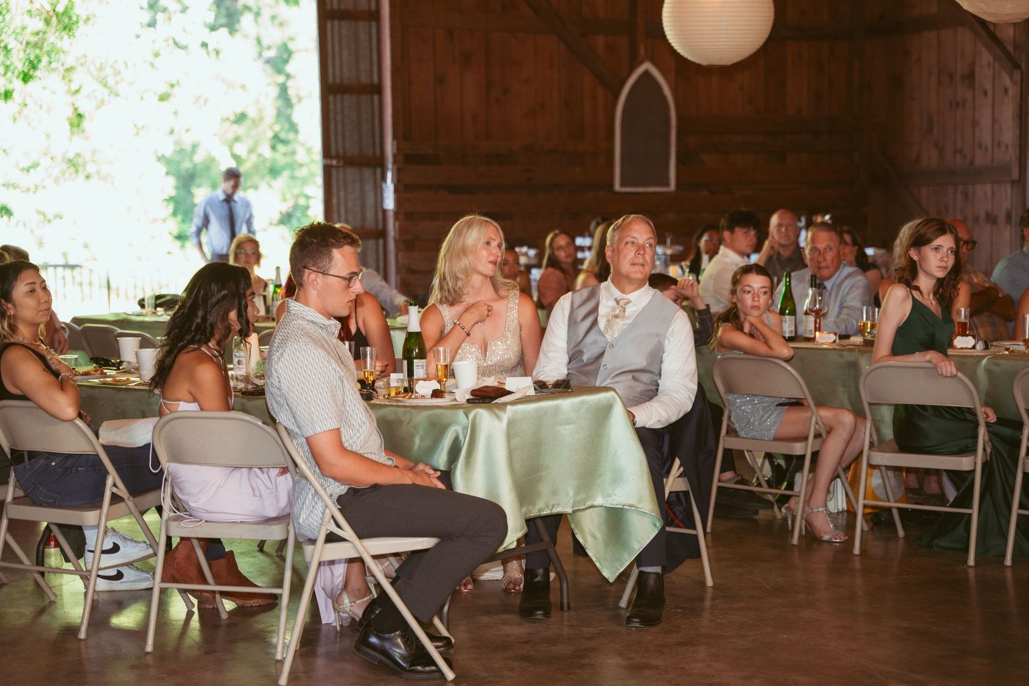 Wedding guests seated at tables during a daytime barn reception with natural lighting.