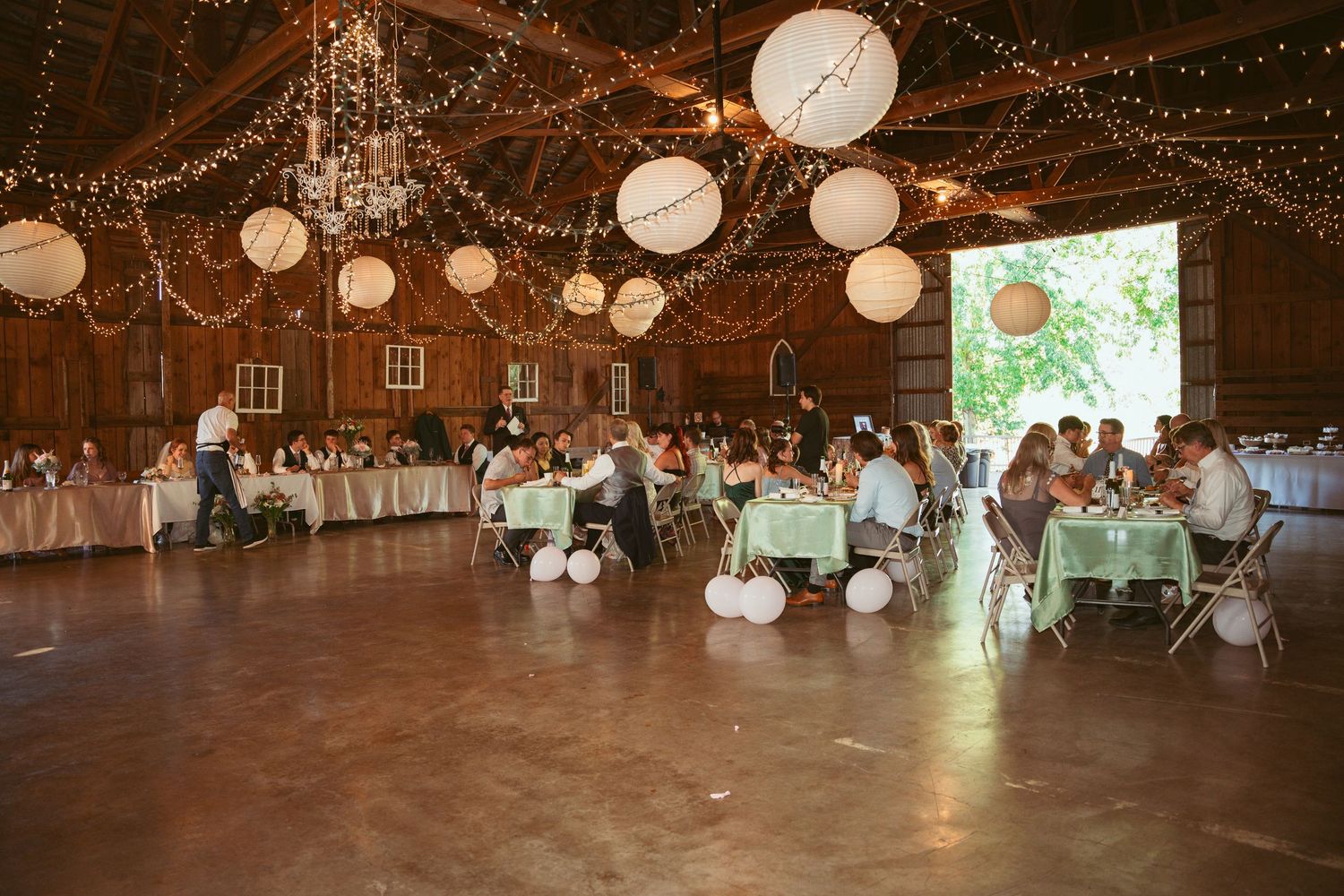 Rustic barn wedding reception with twinkling lights, paper lanterns, and mint green table settings.