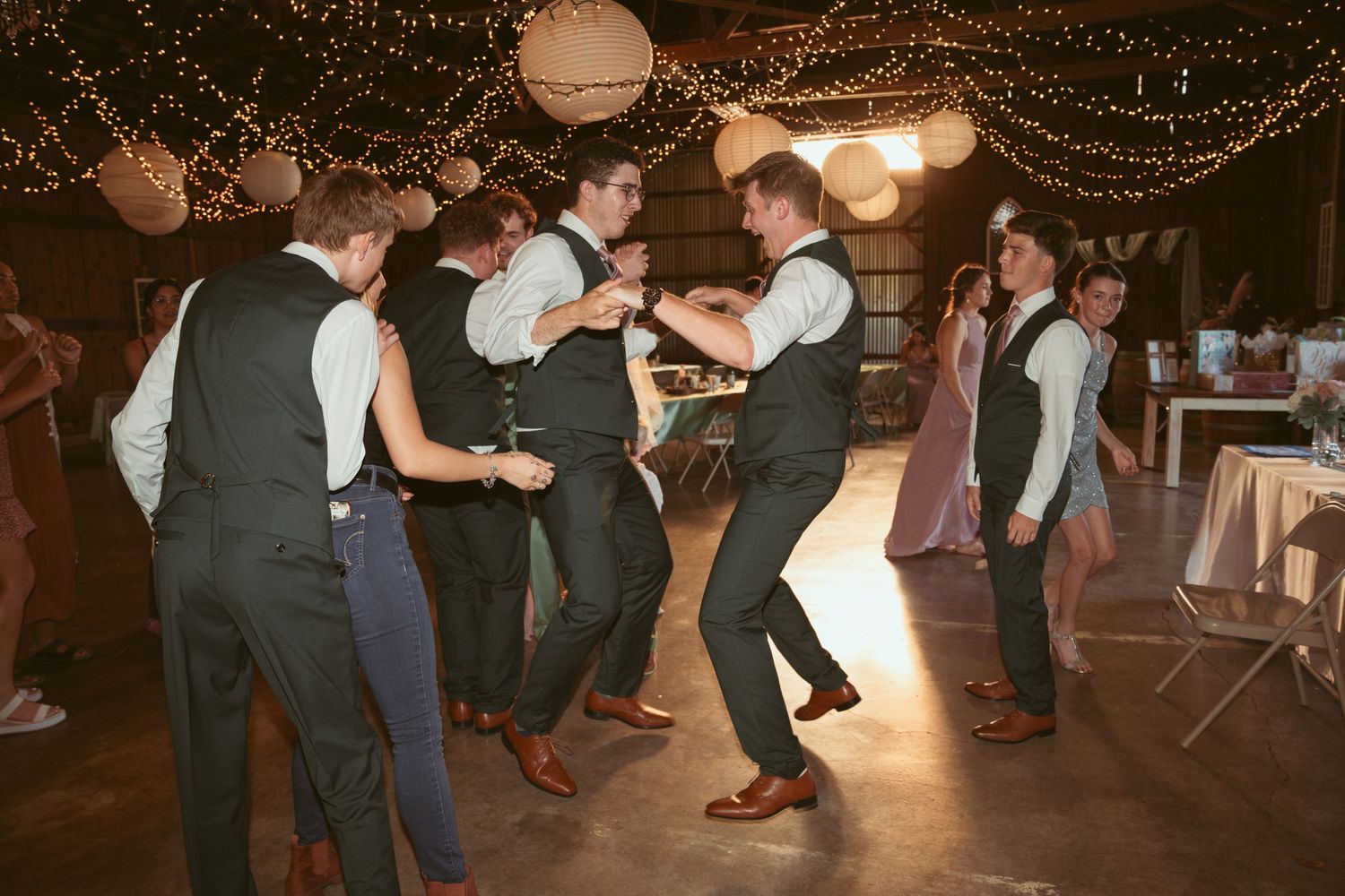 Festive wedding reception dance floor with guests dancing under warm lighting and decorative lanterns.