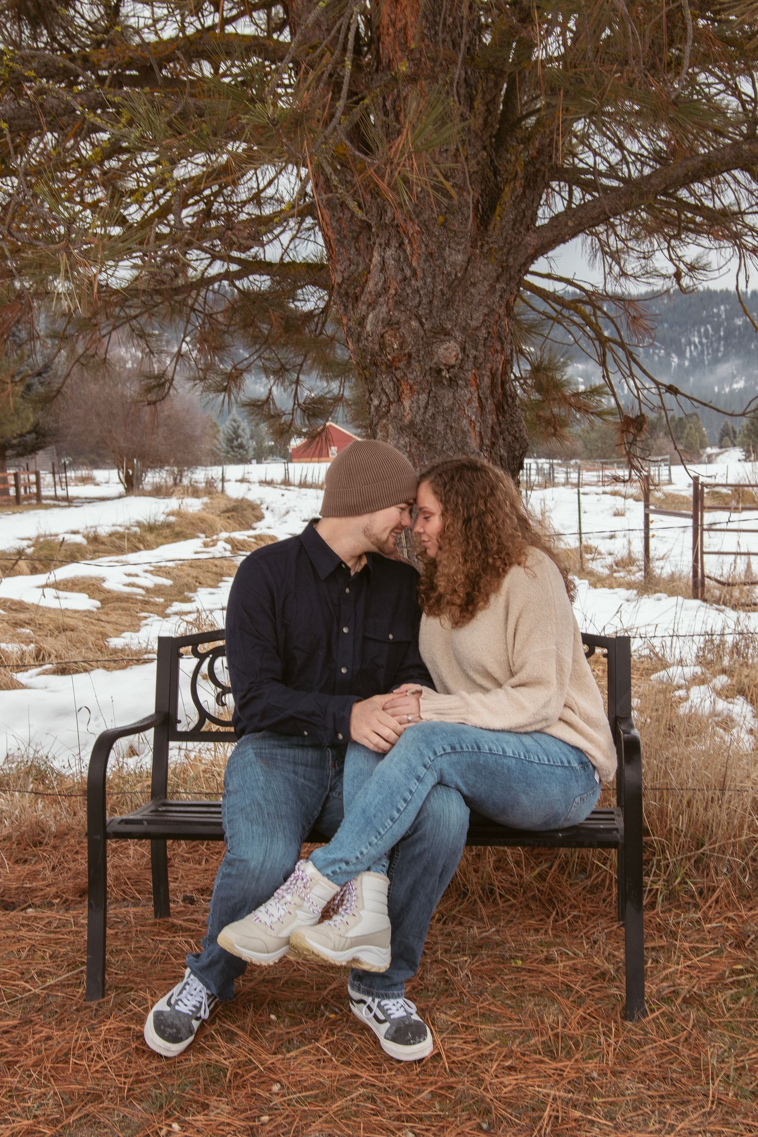 Couple sitting close together on park bench surrounded by winter scenery.