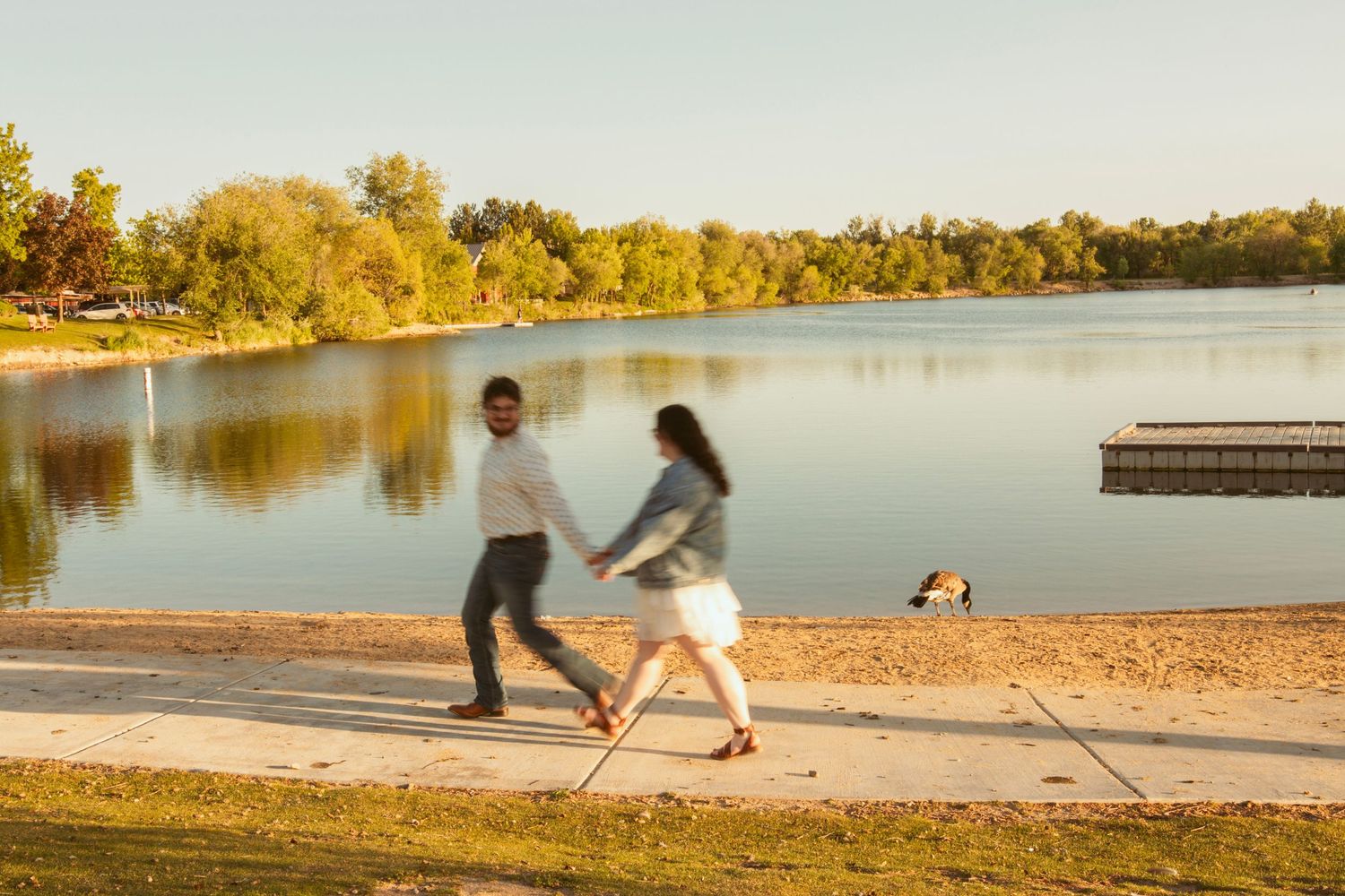 Playful couple running and dancing along a lakeside path at golden hour.