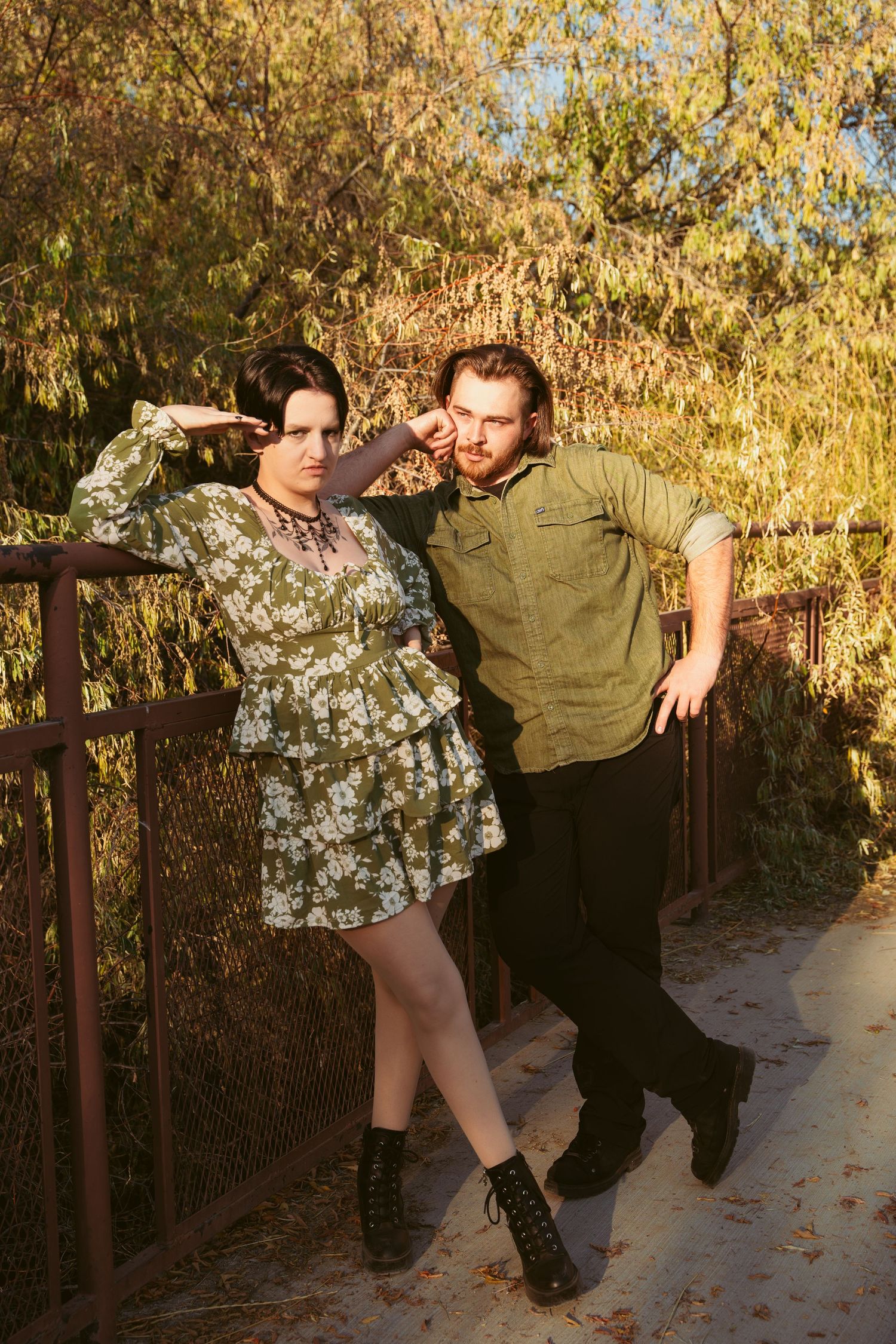 A couple poses playfully on a metal bridge during autumn.