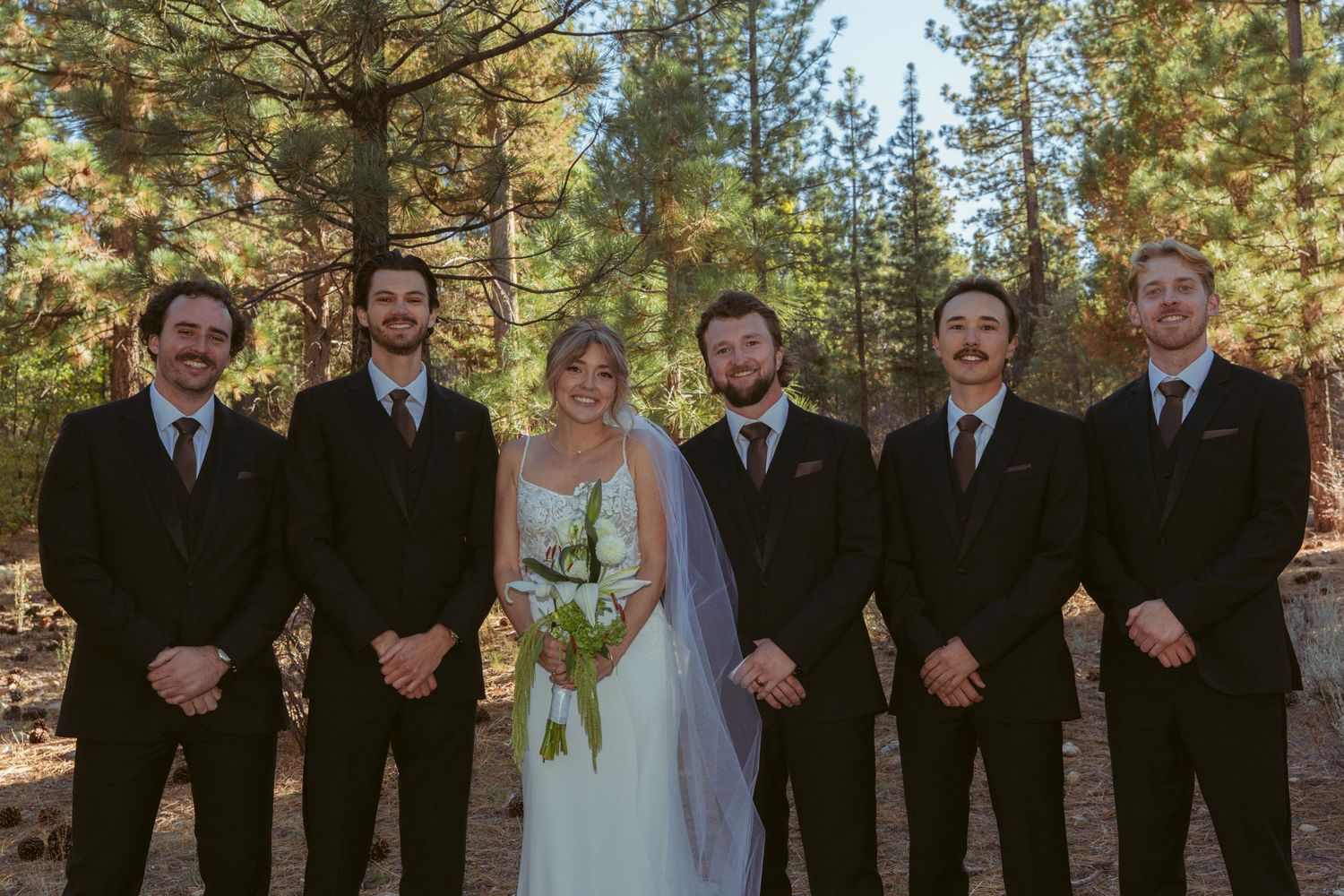 Wedding group photo with formal attire against natural forest backdrop.