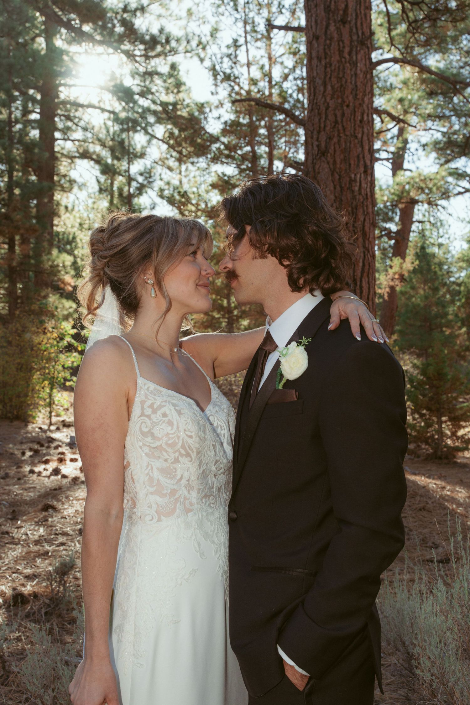 An intimate wedding portrait captured in a forest setting with warm natural light.