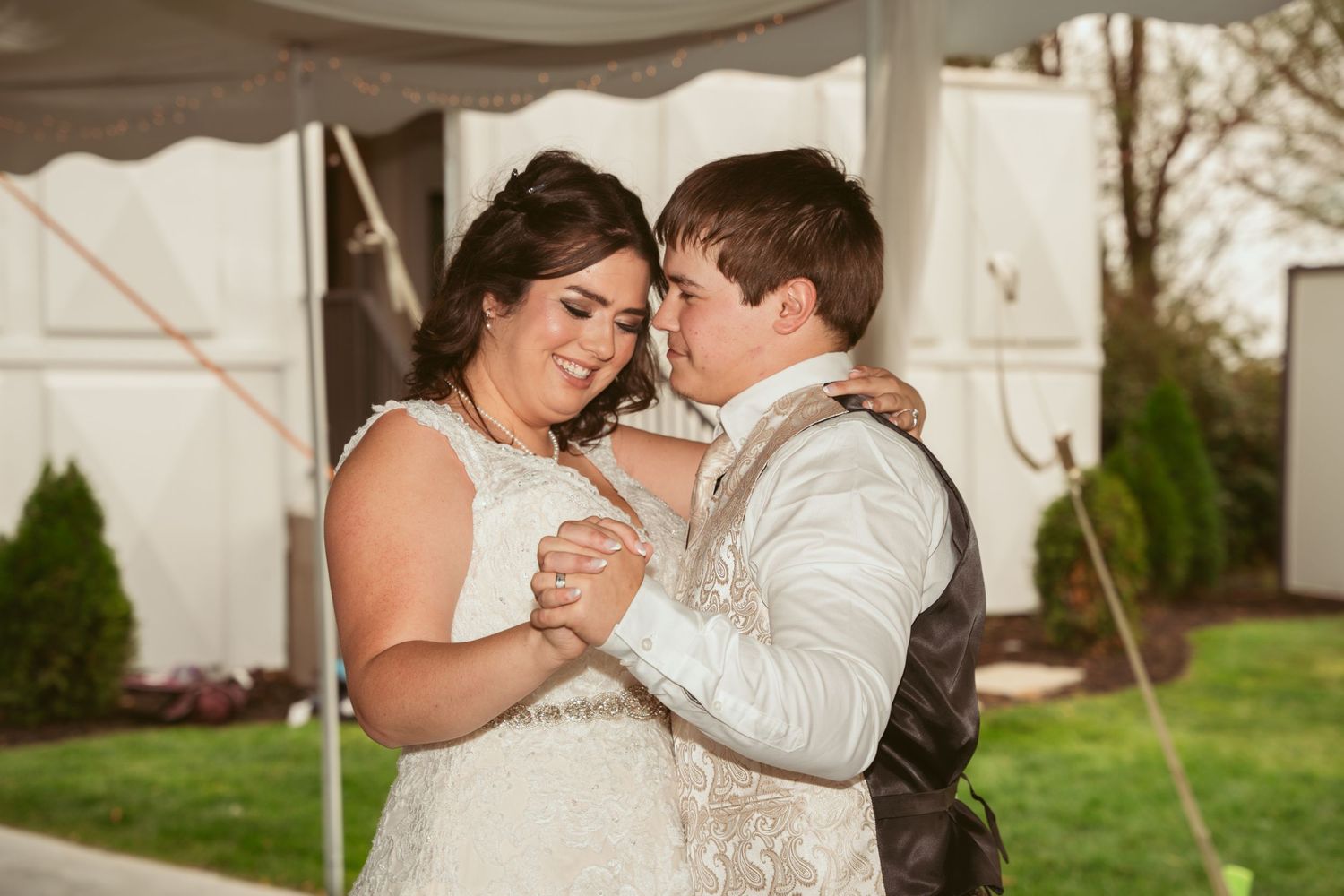 Tender first dance moment under a white tent during an outdoor wedding celebration.