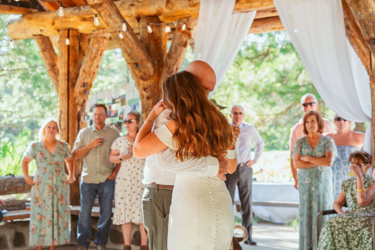 Couple dancing together at a rustic outdoor venue with wooden beams and white drapes.