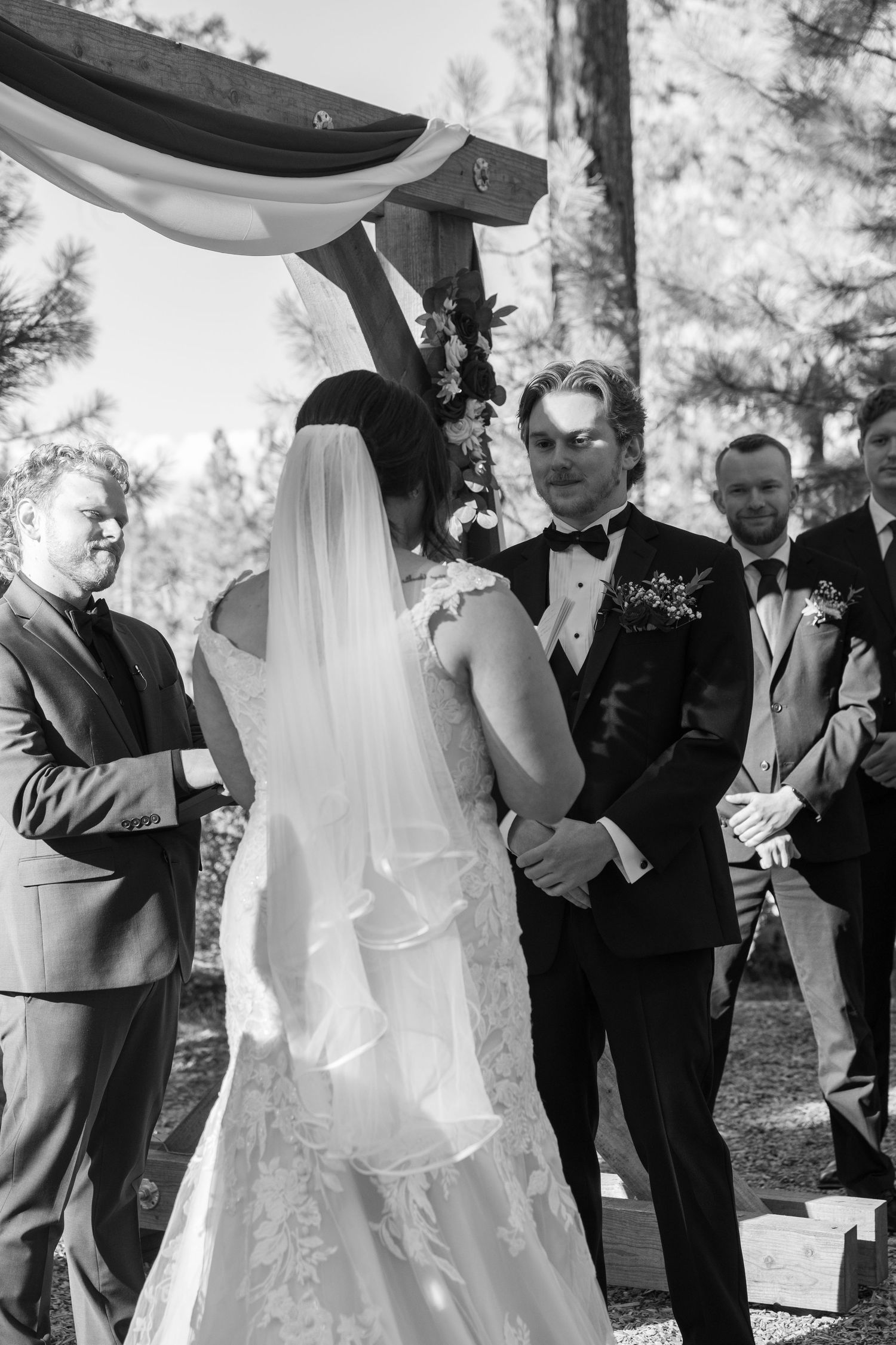 A wedding ceremony taking place outdoors in a forest setting with guests watching the couple exchange vows.