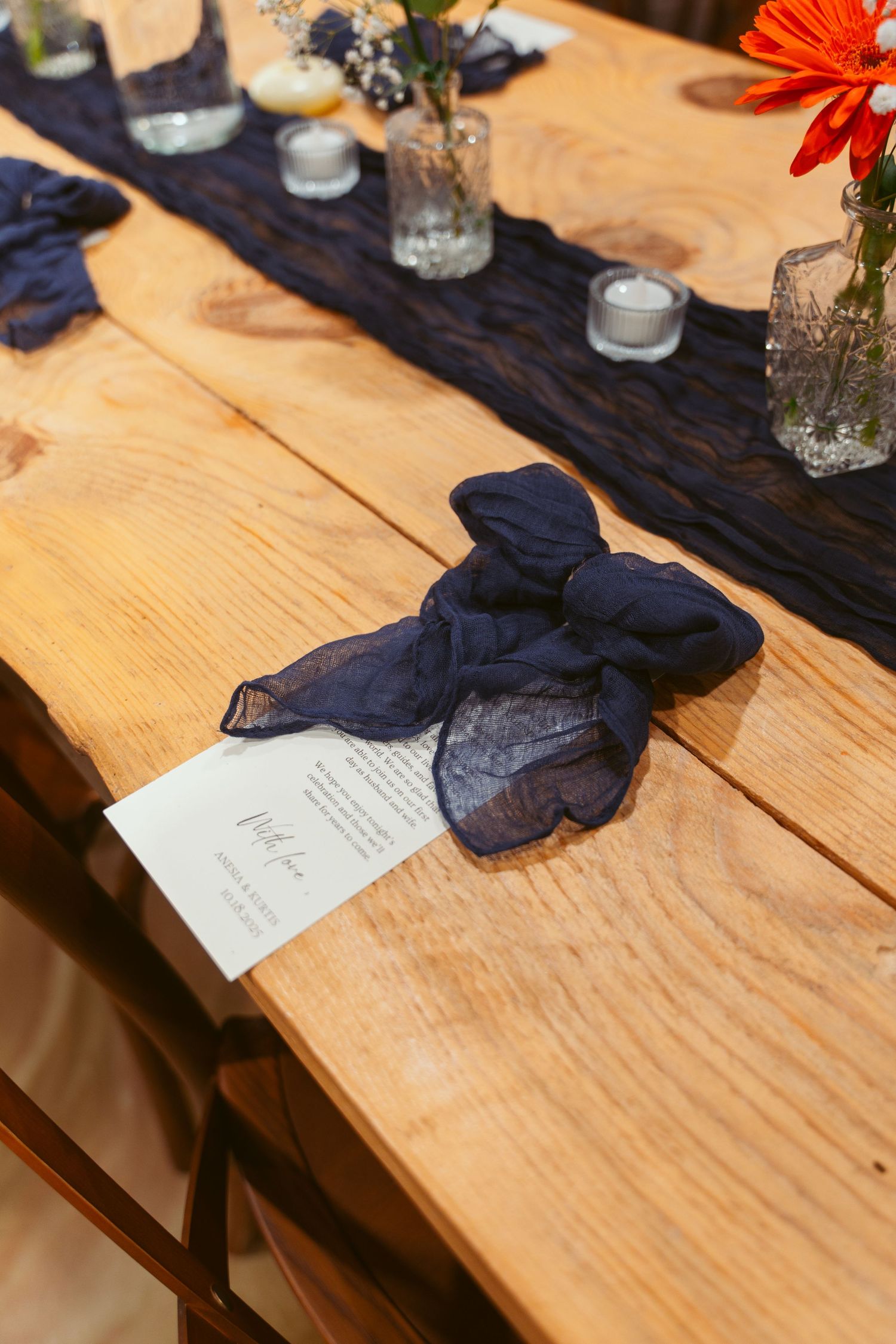 Table setting with navy blue napkins and orange flowers on rustic wooden tables.