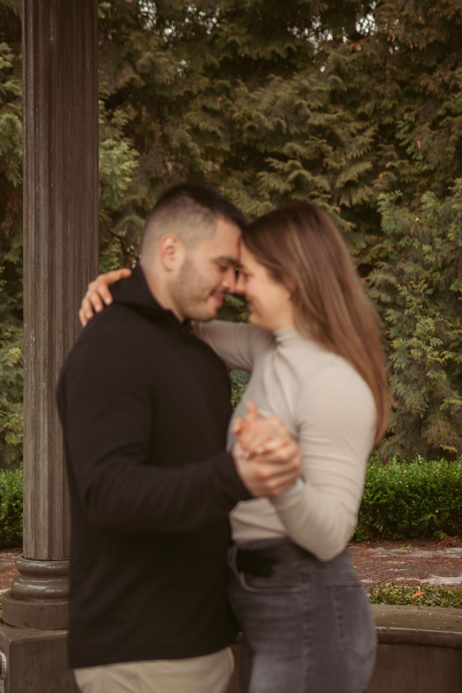 A couple dancing and embracing near stone pillars in a garden setting.