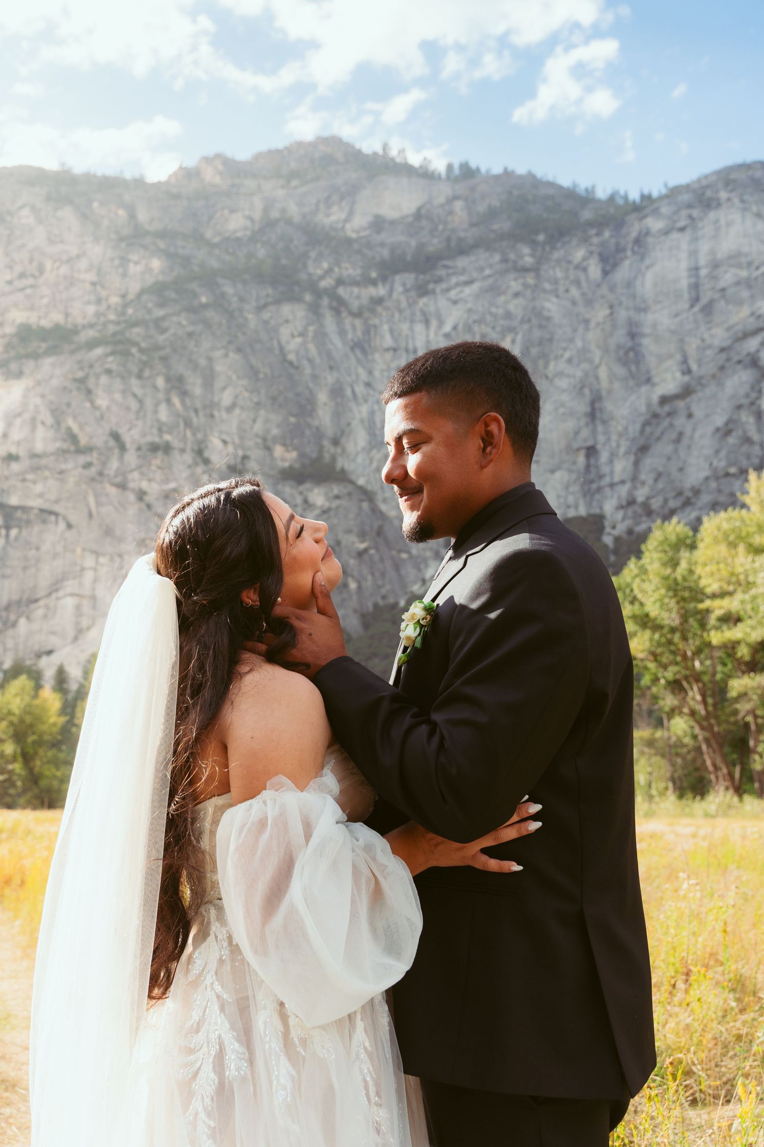 Intimate wedding portrait with towering Yosemite cliffs and meadow in background.