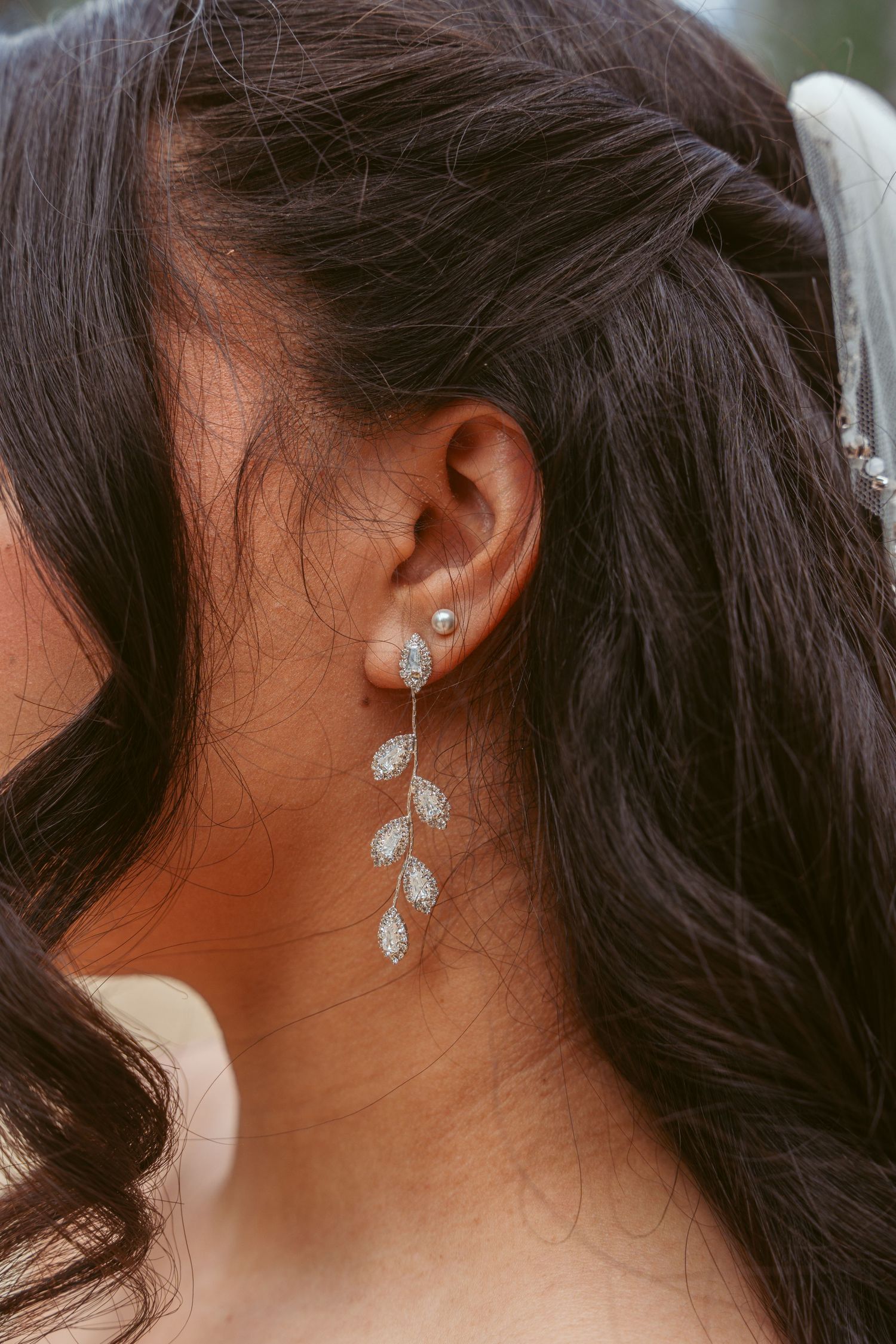 Elegant crystal leaf earrings against dark wavy hair.