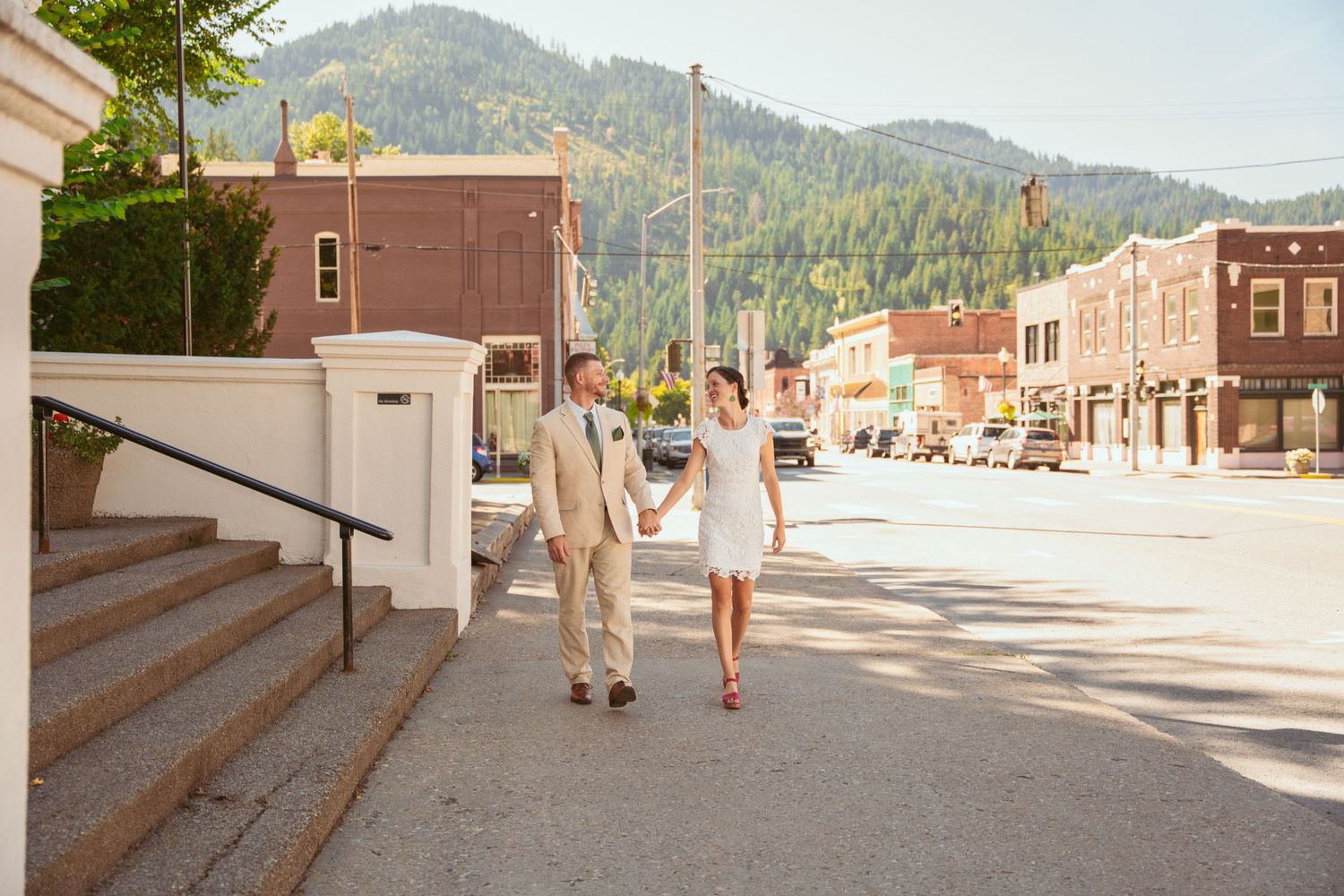 Couple walking hand in hand on a sunny street with mountain views.