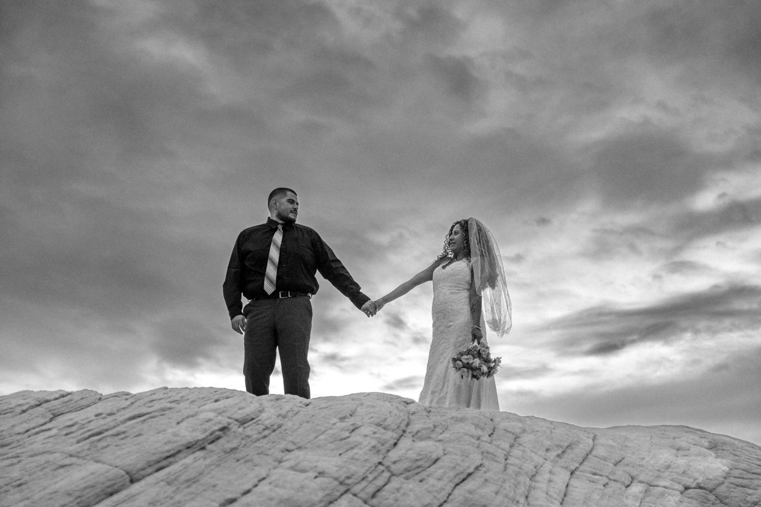 Black and white silhouette of wedding couple standing on dramatic desert landscape.