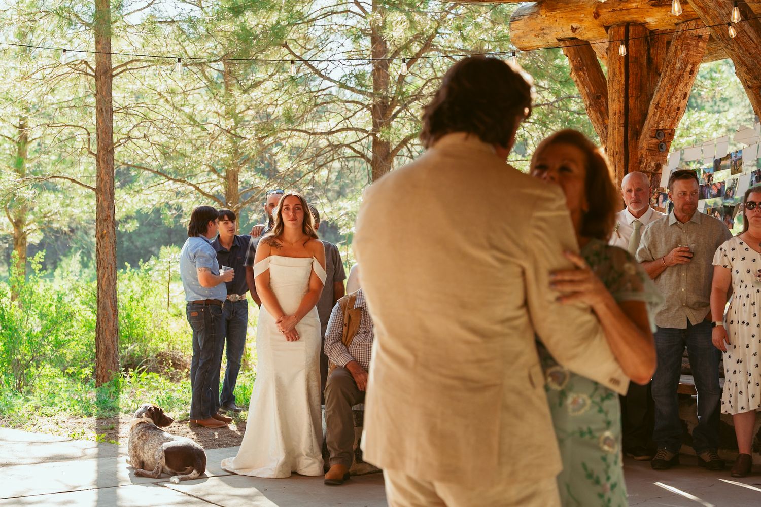 Wedding guests dance and celebrate in a sunlit forest venue with wooden beams.