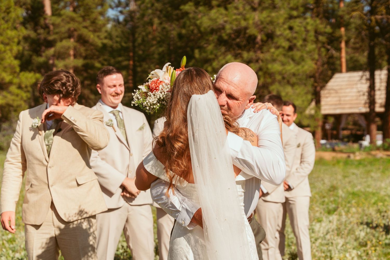 Wedding party members in light colored attire celebrate outdoors in a scenic forest setting.