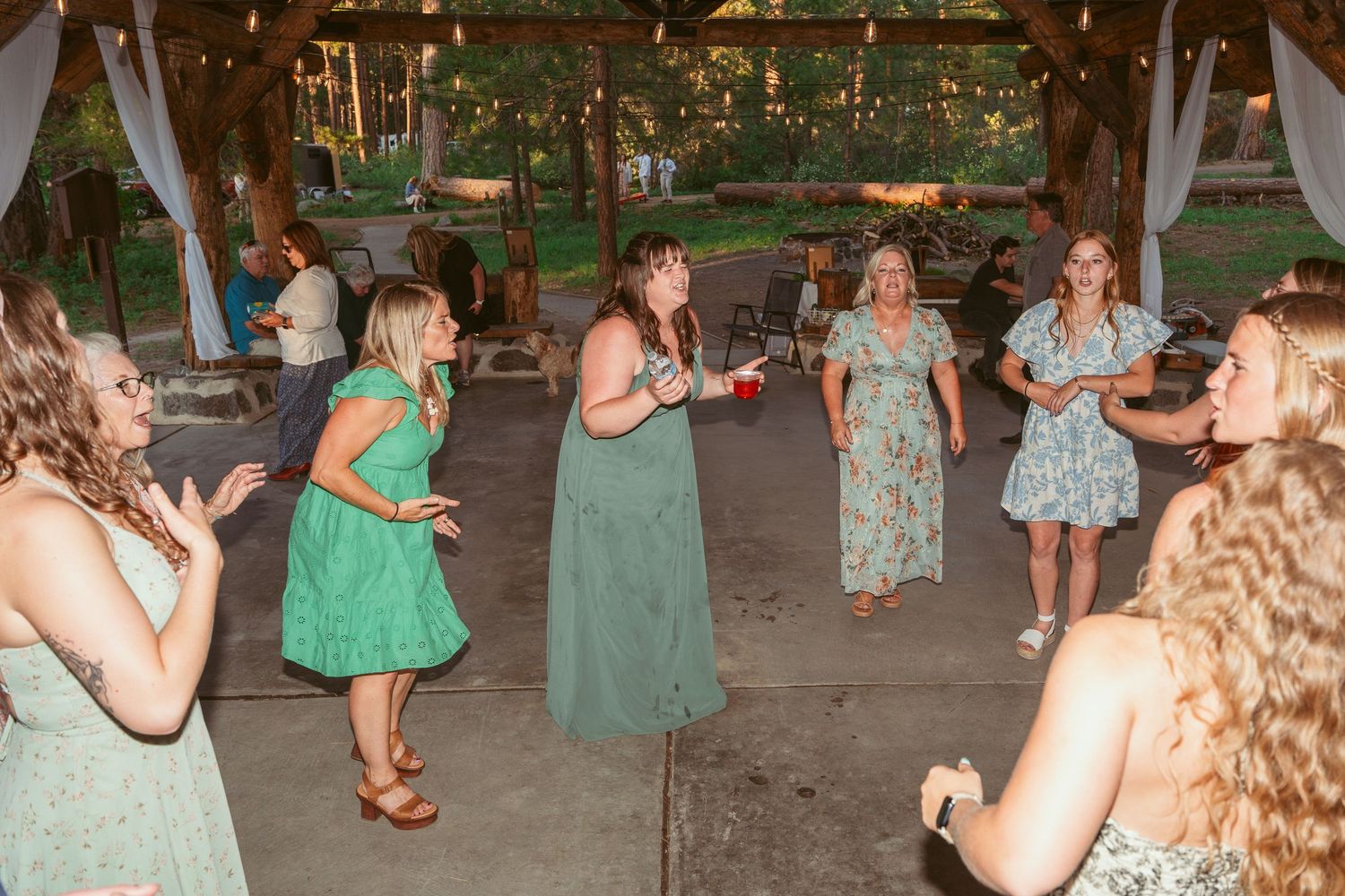 Wedding guests dancing and celebrating under string lights in an outdoor pavilion.