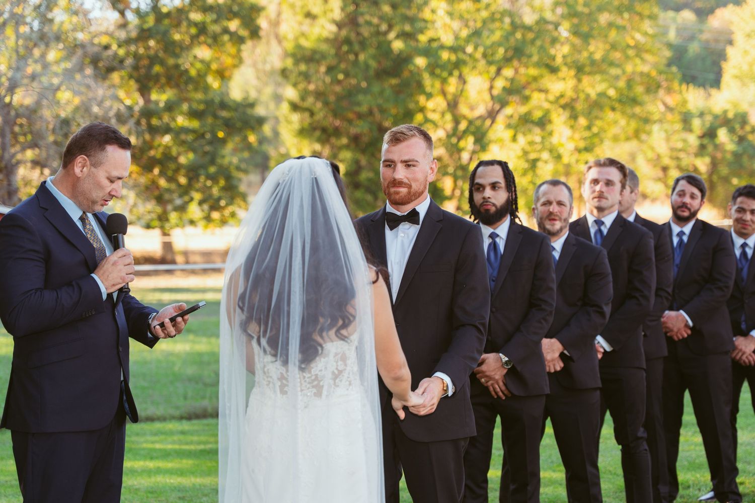 Wedding party gathered outdoors with autumn trees and formal attire.