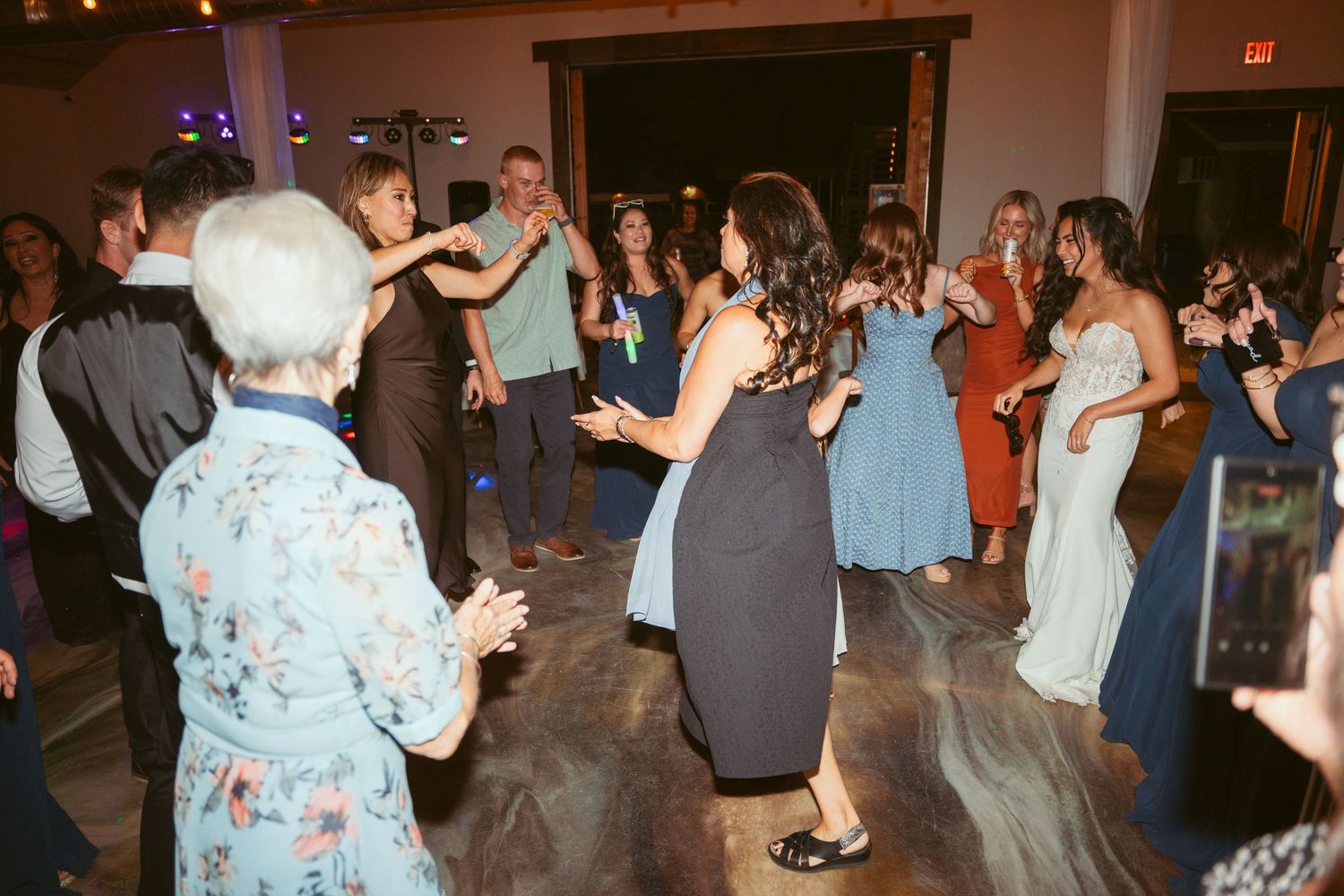 Celebration in full swing with guests dancing under decorative string lights at an indoor venue.