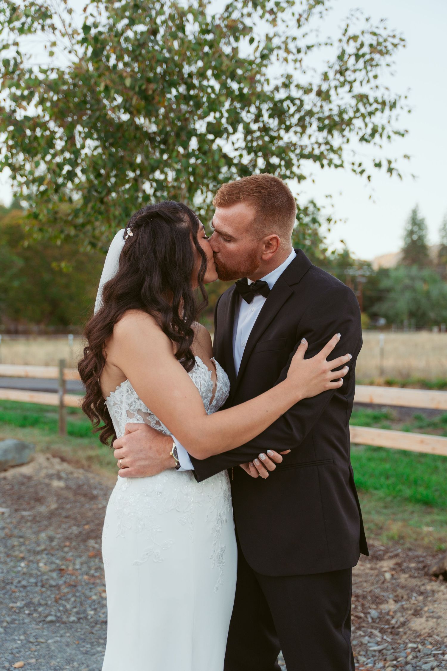 Newlyweds embrace tenderly against a backdrop of fall foliage and trees.