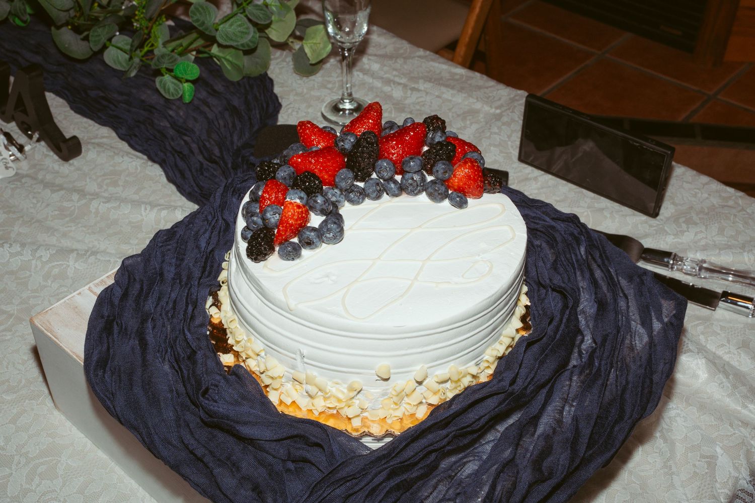 A white wedding cake decorated with orange and red flowers sits atop a navy blue tablecloth.