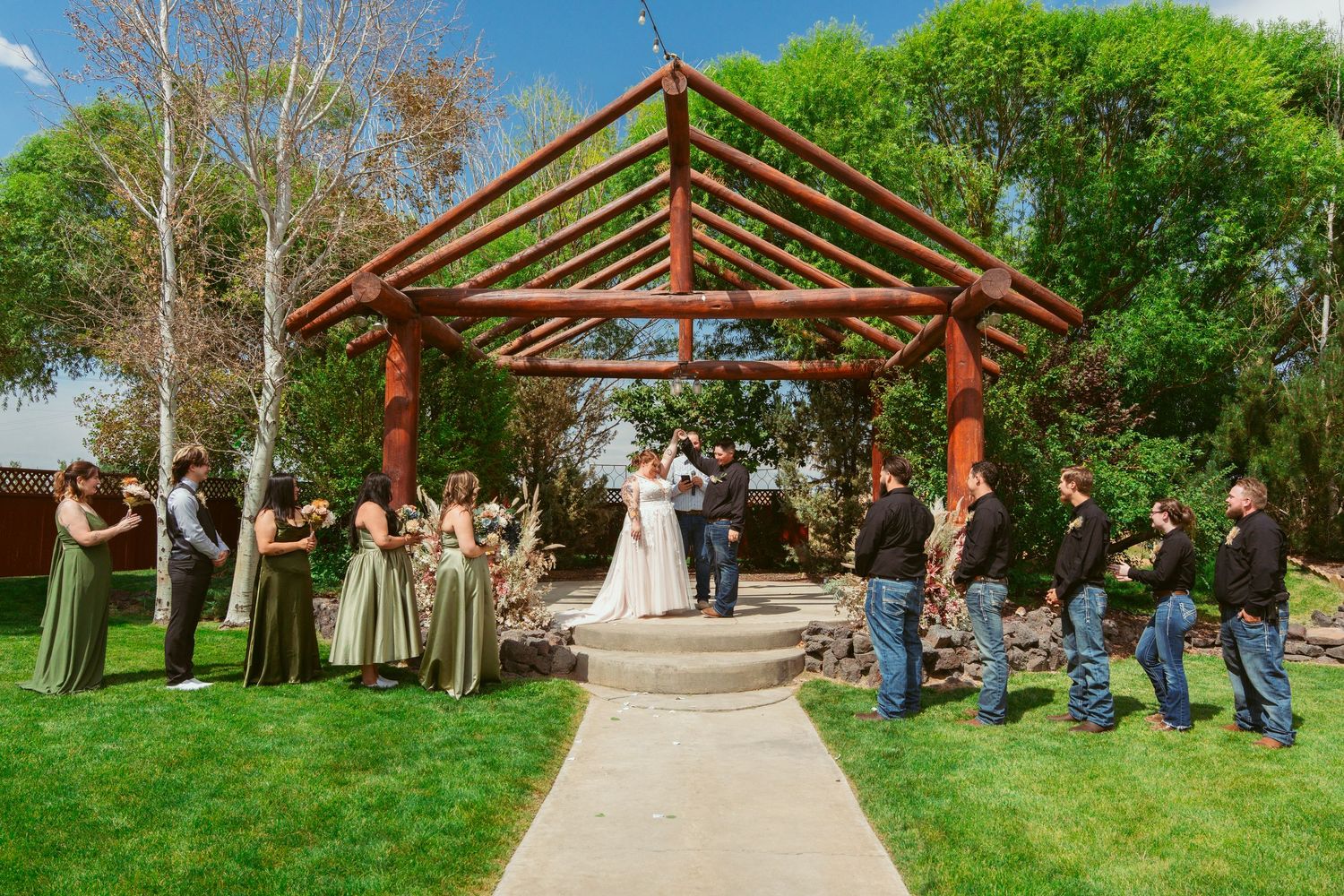 Outdoor wedding ceremony venue with wooden pergola and white chairs arranged on grass under clear skies.