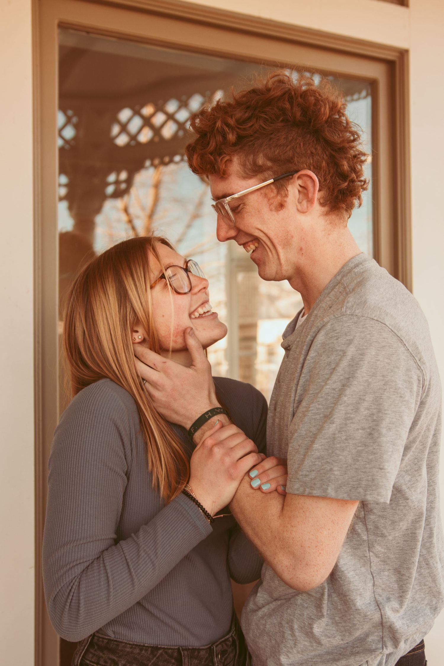A couple shares an intimate moment together in front of a window with warm lighting.