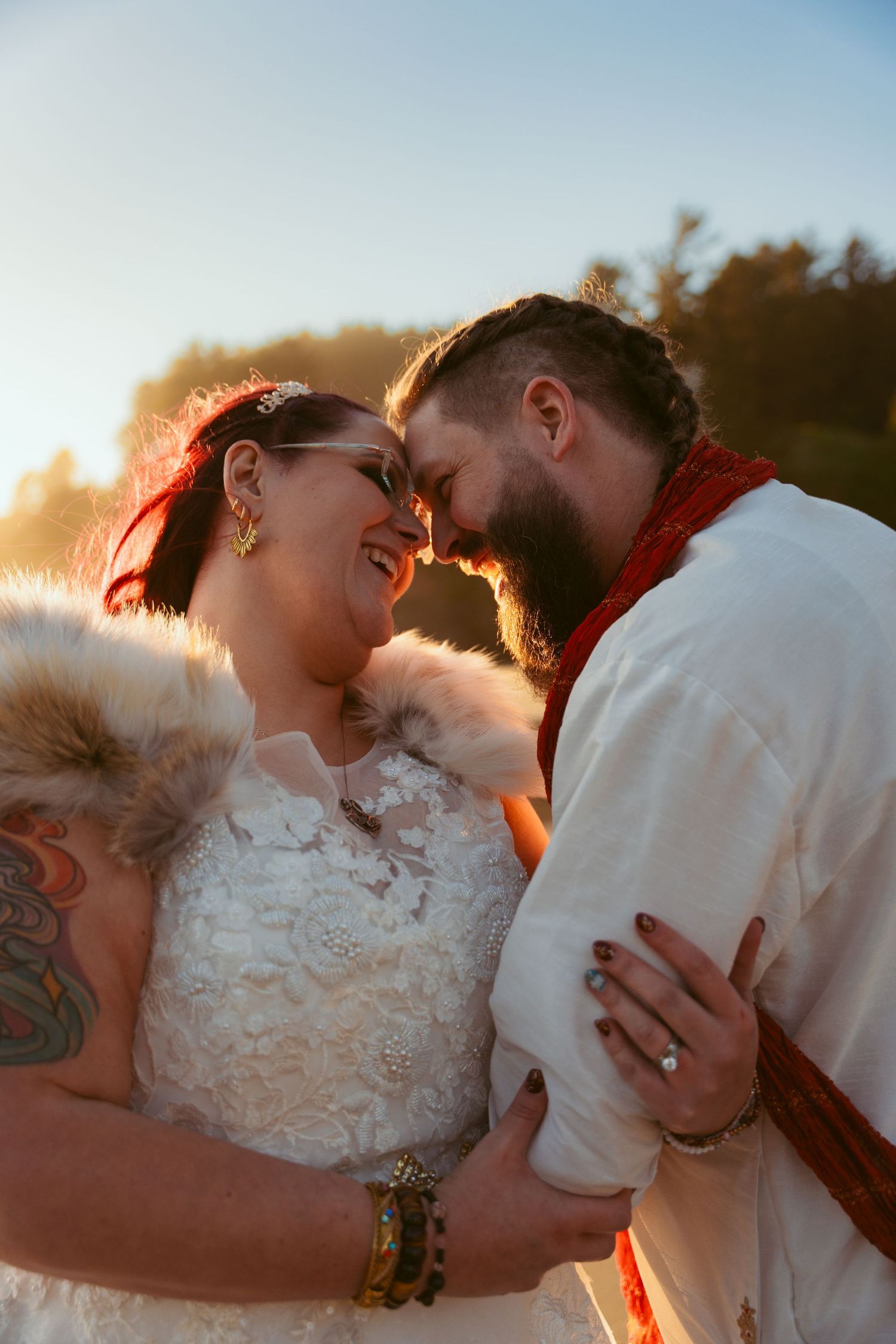 Romantic sunset wedding portrait with couple in white attire sharing tender moment.