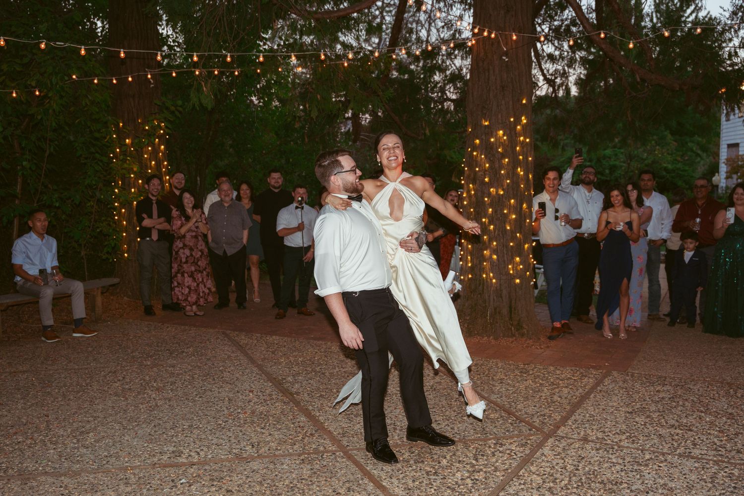 A couple performs their first dance at an outdoor wedding reception under string lights.