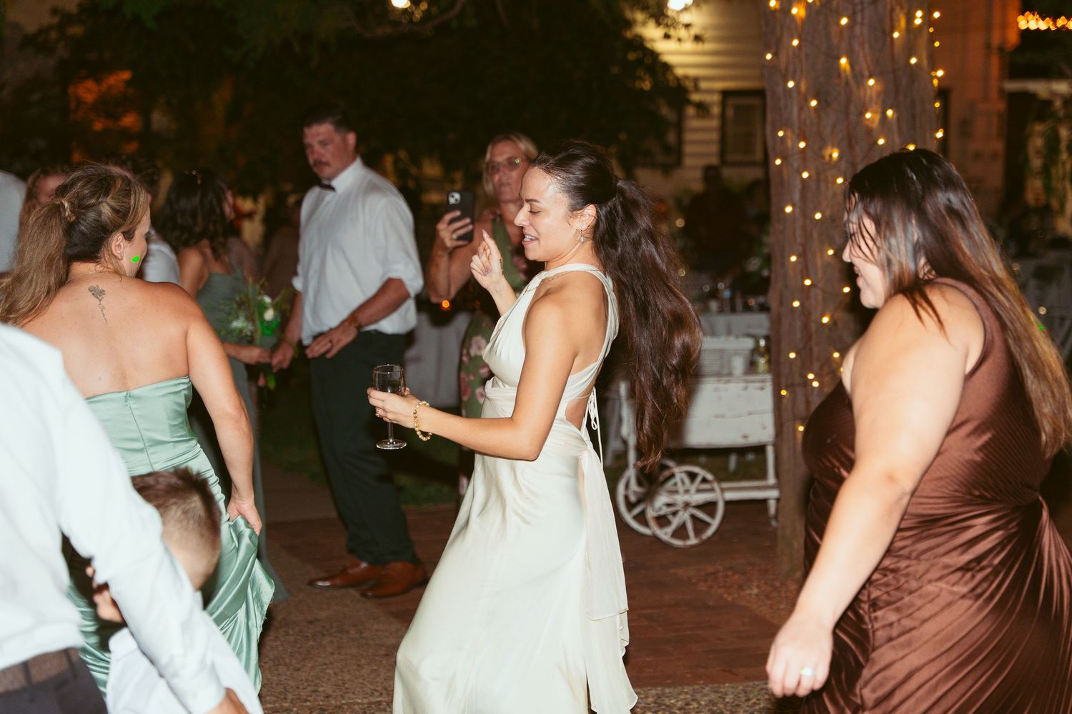 Wedding reception dance party under warm string lights in an outdoor venue.