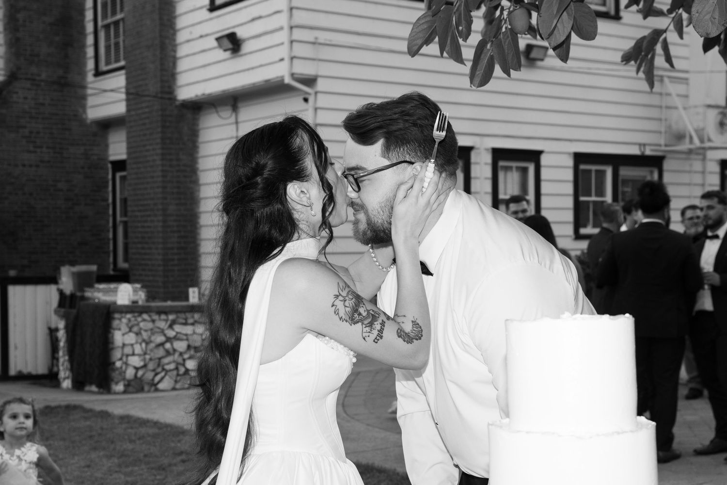 Wedding couple shares romantic moment outside traditional white clapboard building.