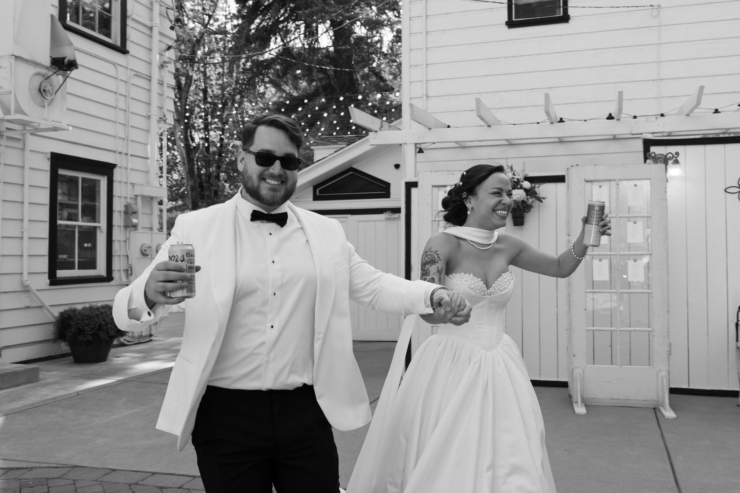 Outdoor wedding reception with guests dancing on a patio near a white building.