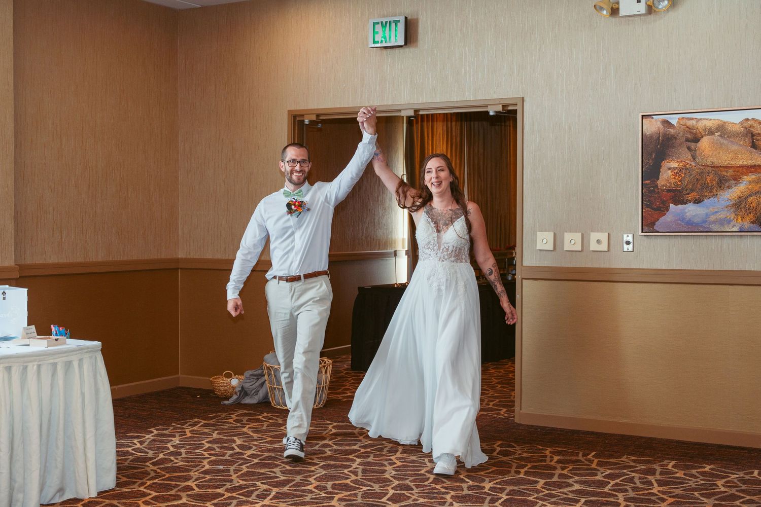 Couple in white wedding attire dancing together in an empty reception hall with wood paneled walls.