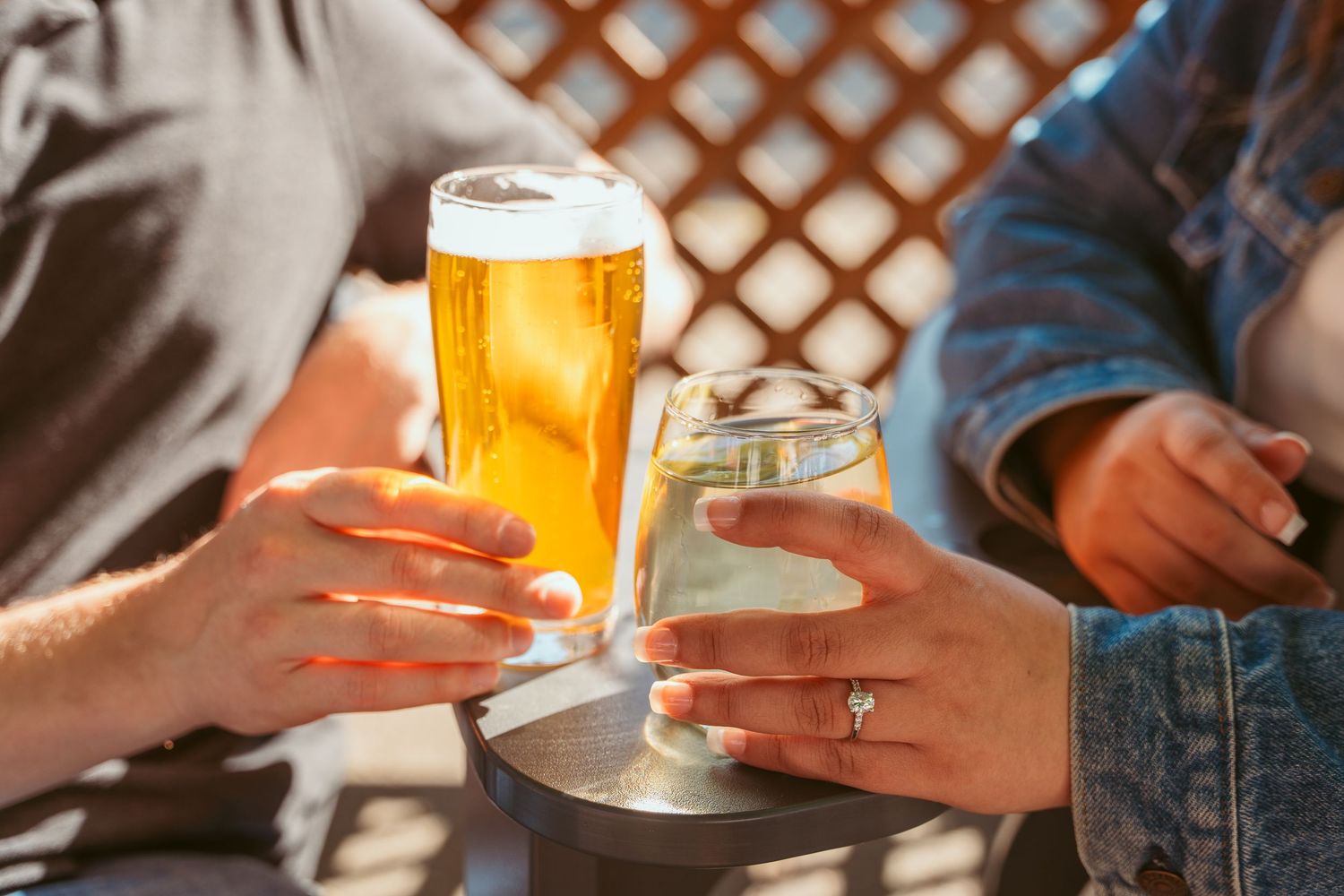 Close-up of hands toasting with golden beer glasses on wooden table.