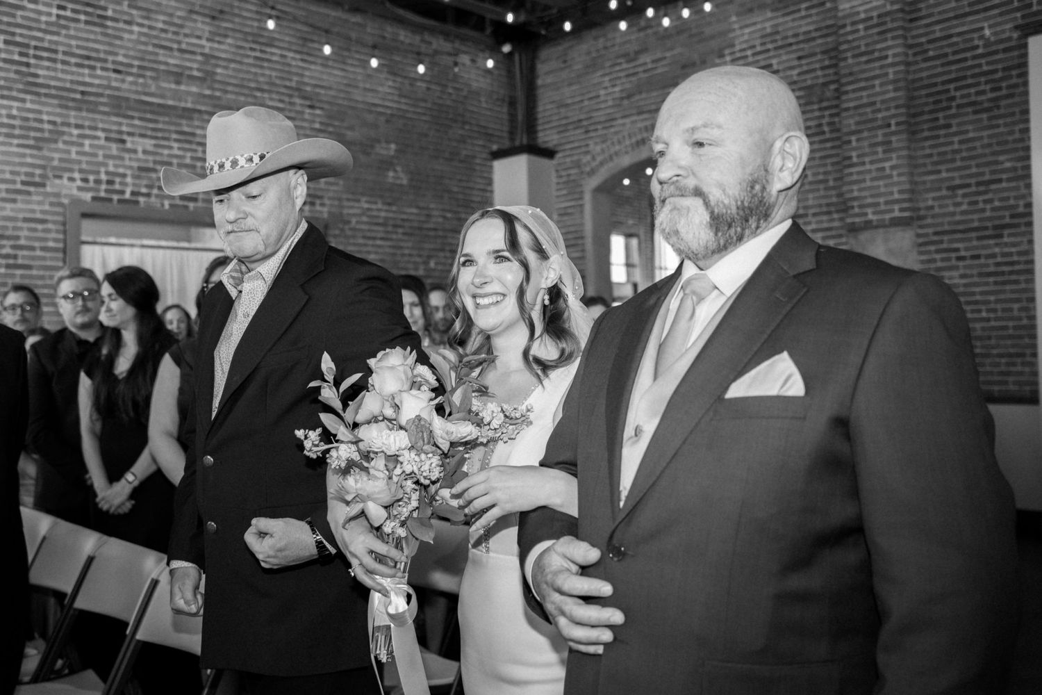 Wedding guests dancing and celebrating at an indoor reception with exposed brick walls and string lights.