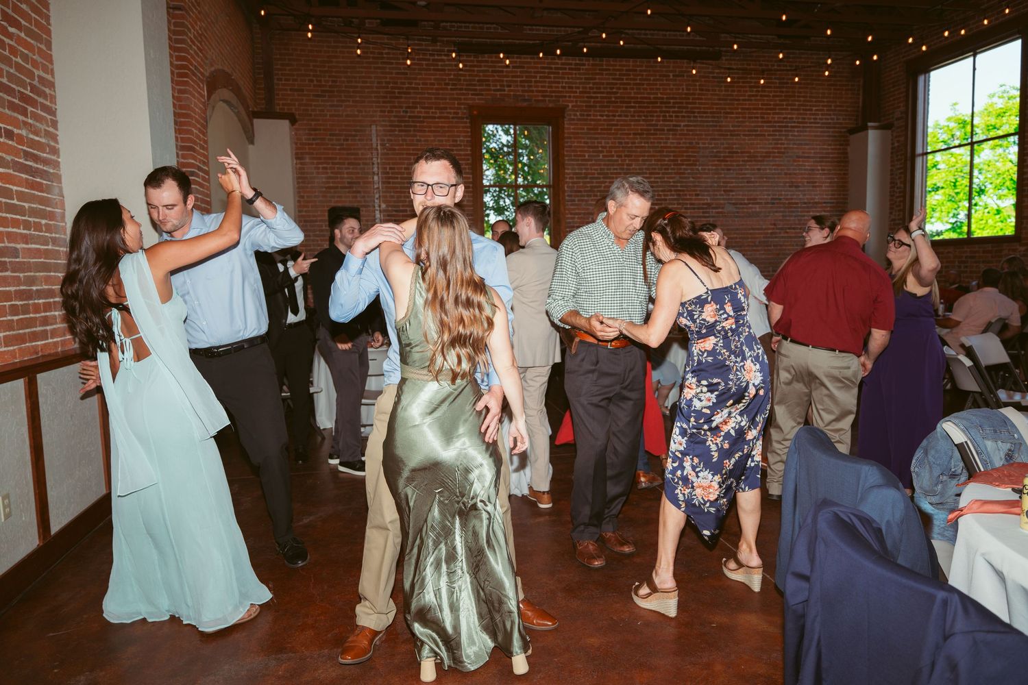 Wedding celebration with people dancing in a rustic brick-walled venue decorated with string lights.