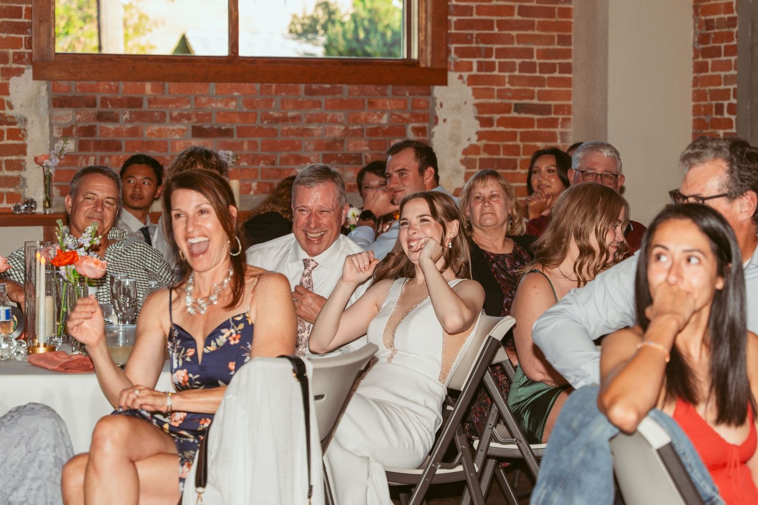 Wedding guests enjoying the celebration in a spacious brick venue with large windows.