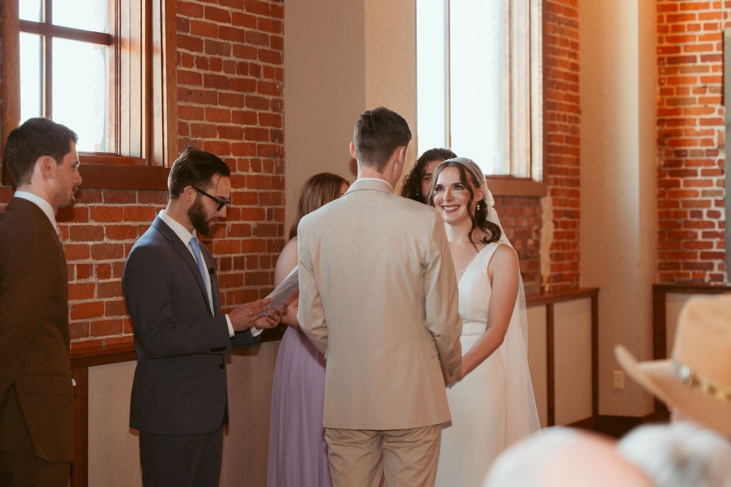 Intimate wedding ceremony moment captured in rustic brick venue with natural light.