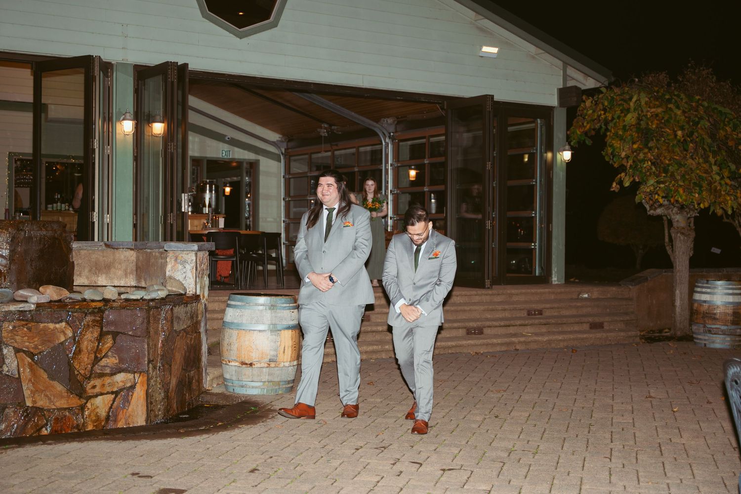 Wedding attendees in formal attire walk along a brick paved pathway at night.