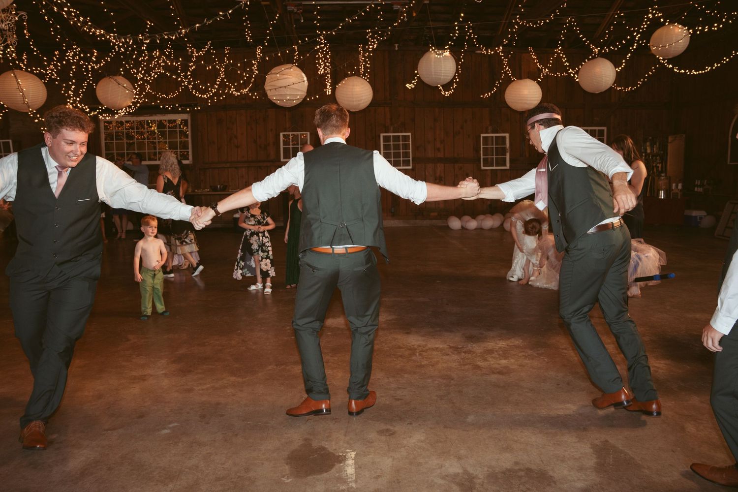 Wedding guests performing synchronized dance moves under rustic barn lighting.