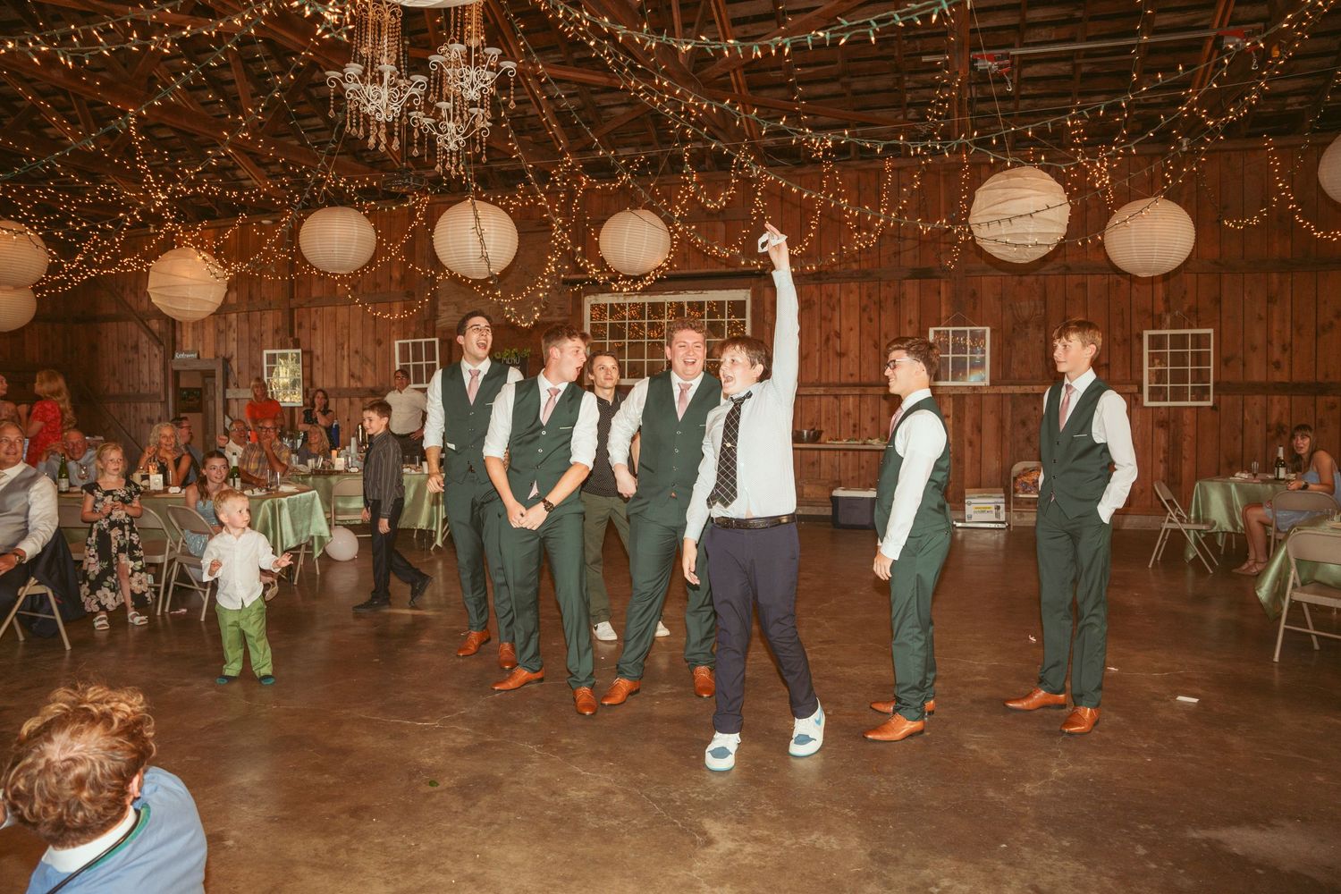 Wedding guests dance in a rustic barn venue decorated with string lights and paper lanterns.