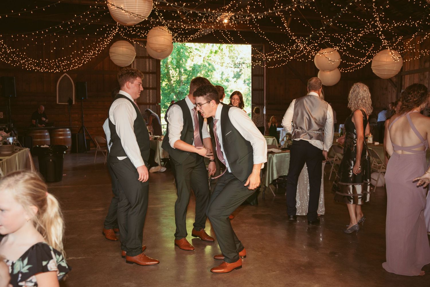 Guests in formal attire dancing and celebrating at a rustic barn wedding reception.