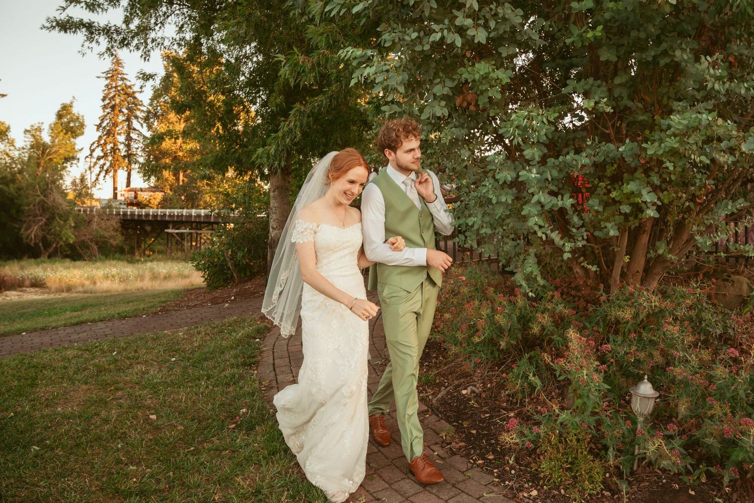 Couple walks together on garden path during golden hour at outdoor wedding venue.