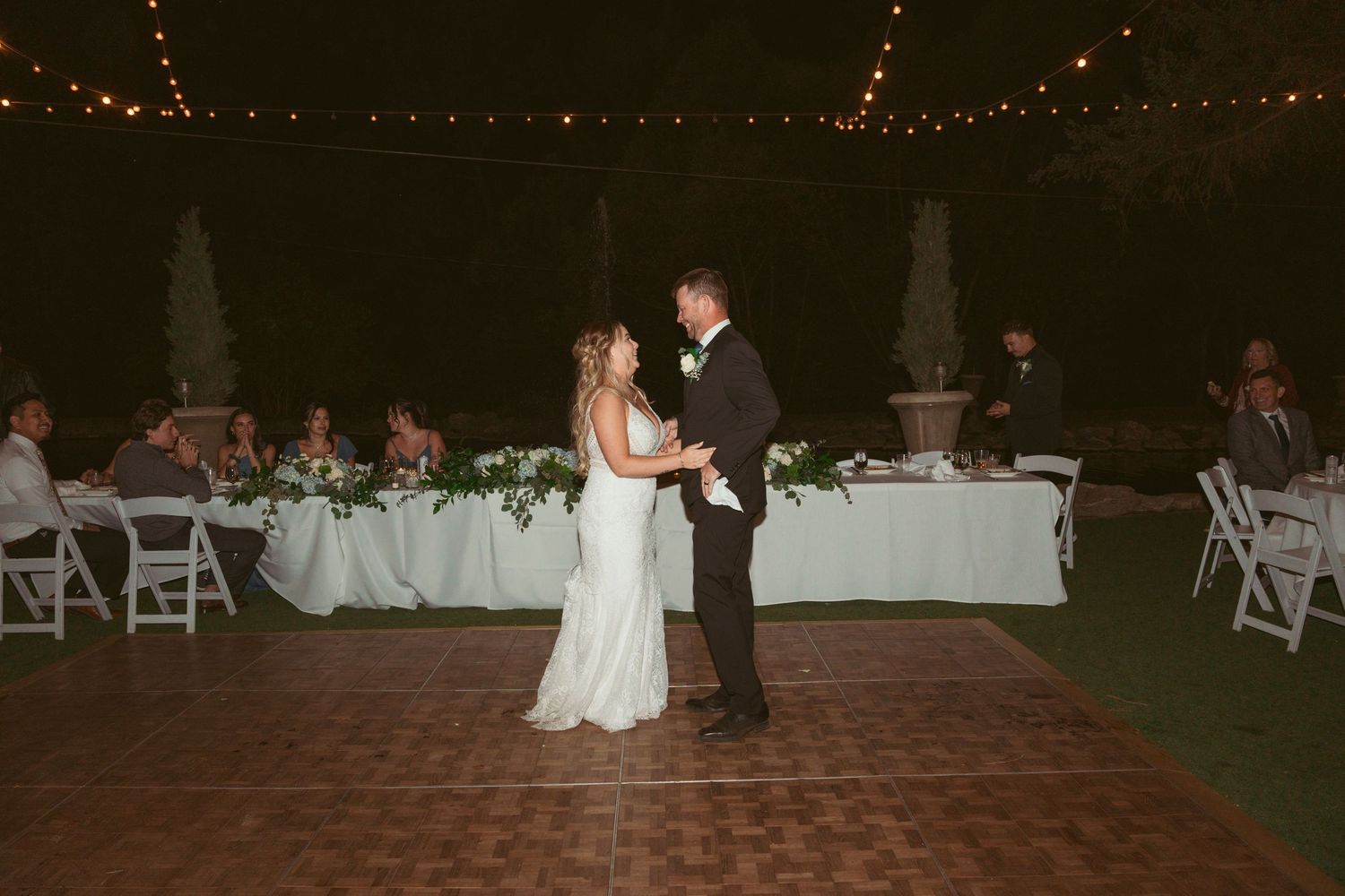 Outdoor wedding reception at night with string lights illuminating the dance floor.