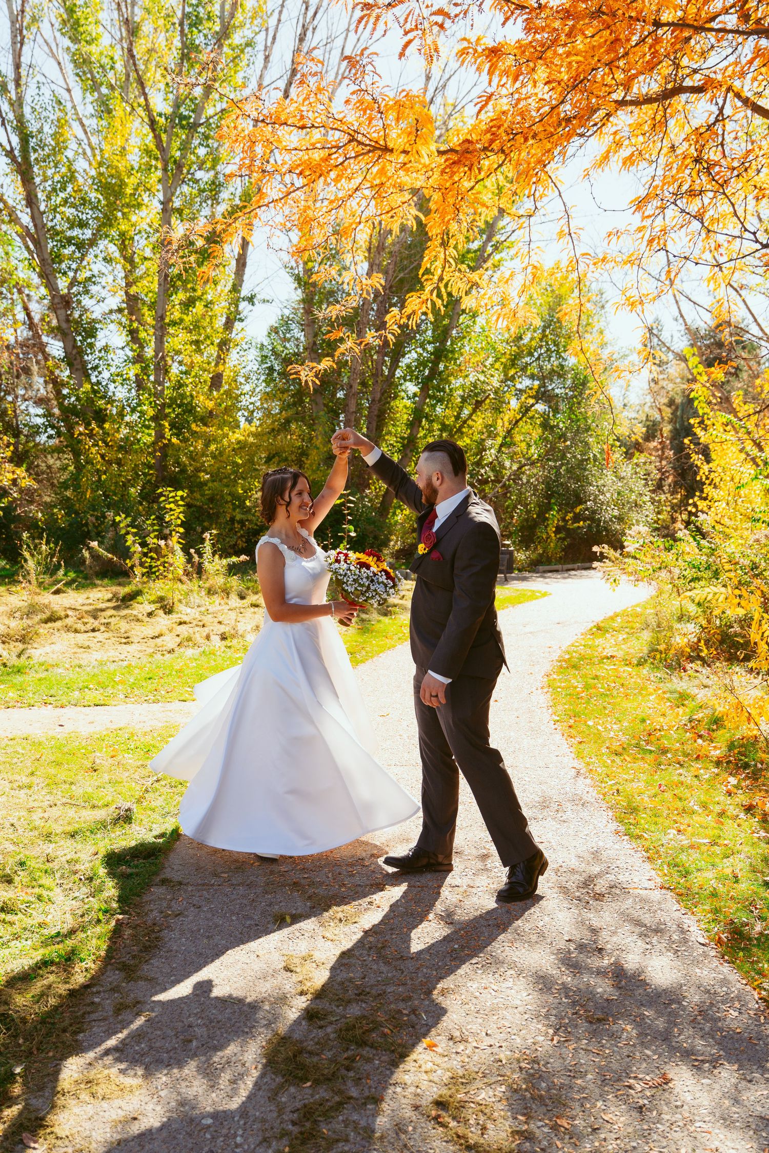 A couple twirls together on a forest trail with vibrant fall colors in the background.