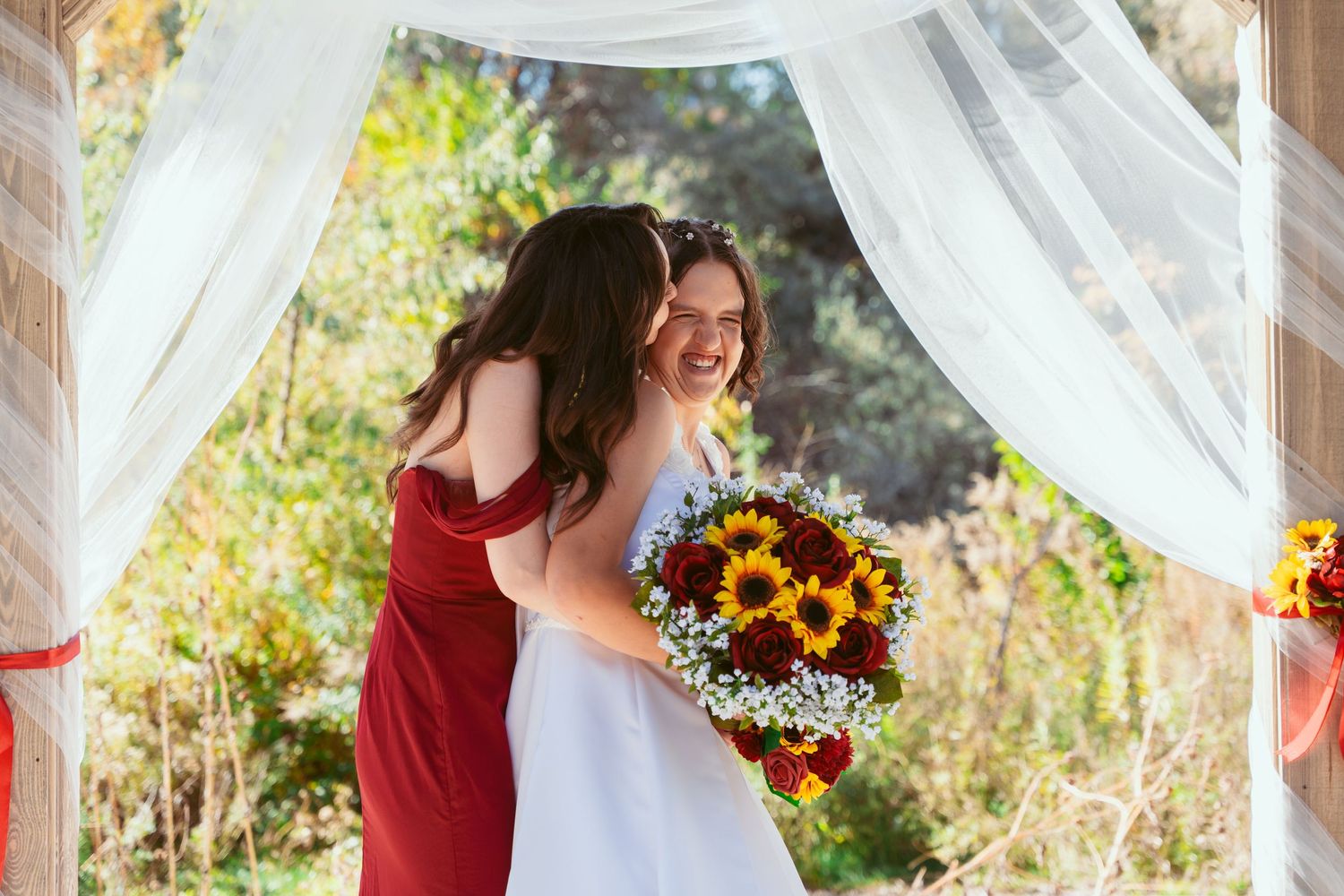 Wedding celebration with sunflower bouquets and burgundy accents under outdoor pavilion.