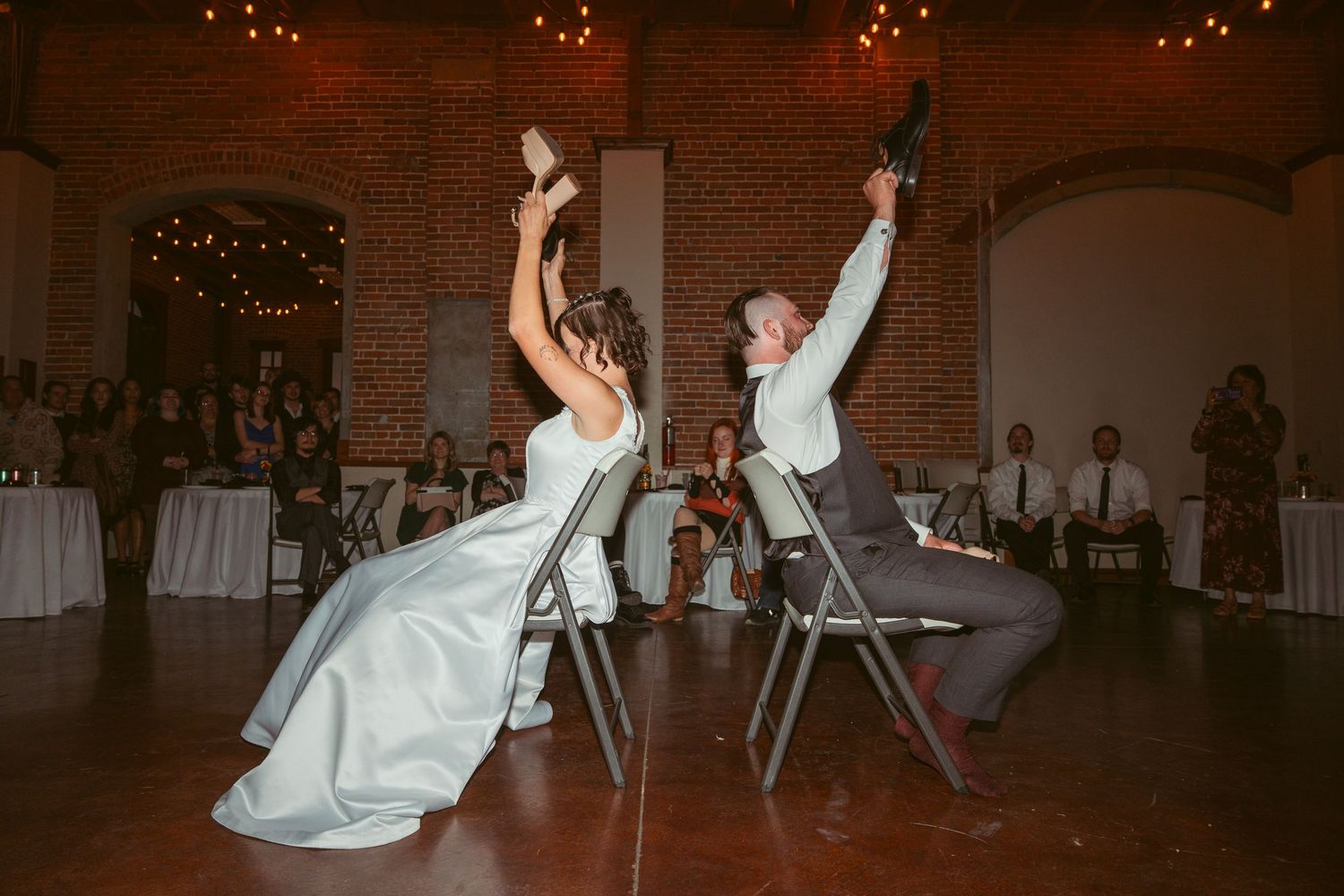 Wedding dancers perform synchronized moves on a wooden floor under string lights.