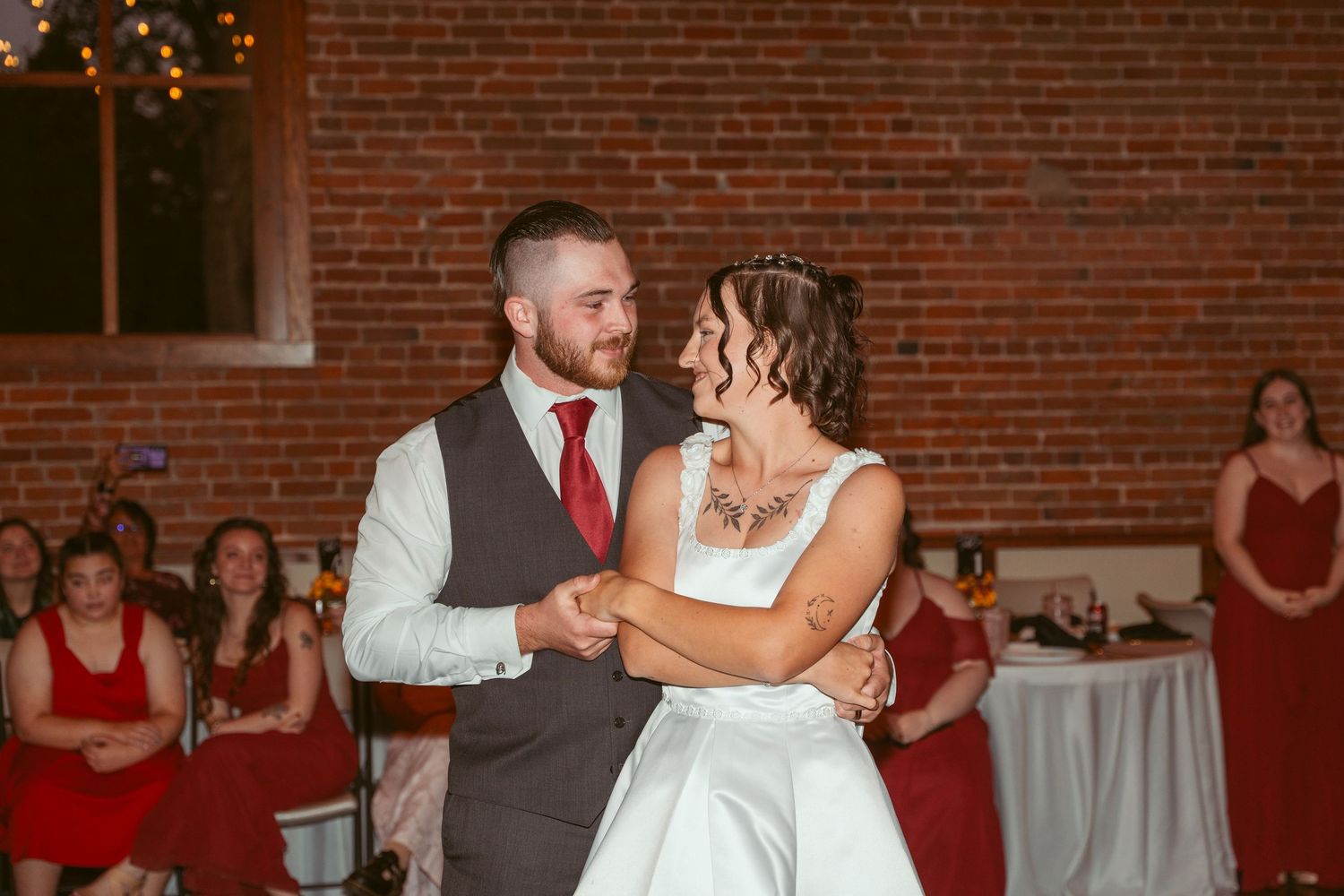 Newlyweds dancing together in an elegant reception hall with exposed brick walls and ambient lighting.