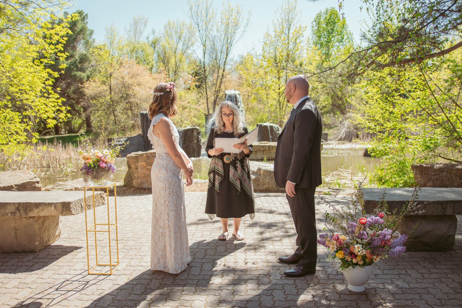 Wedding ceremony taking place outdoors in a garden setting with spring blossoms and greenery.
